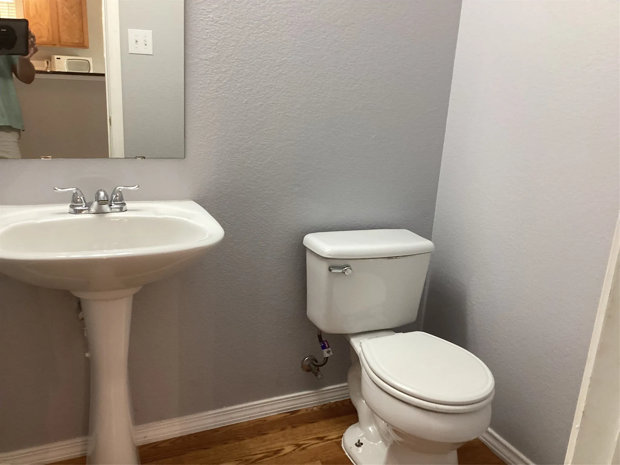 Pedestal sink with chrome faucet, white toilet, and wood-finish flooring