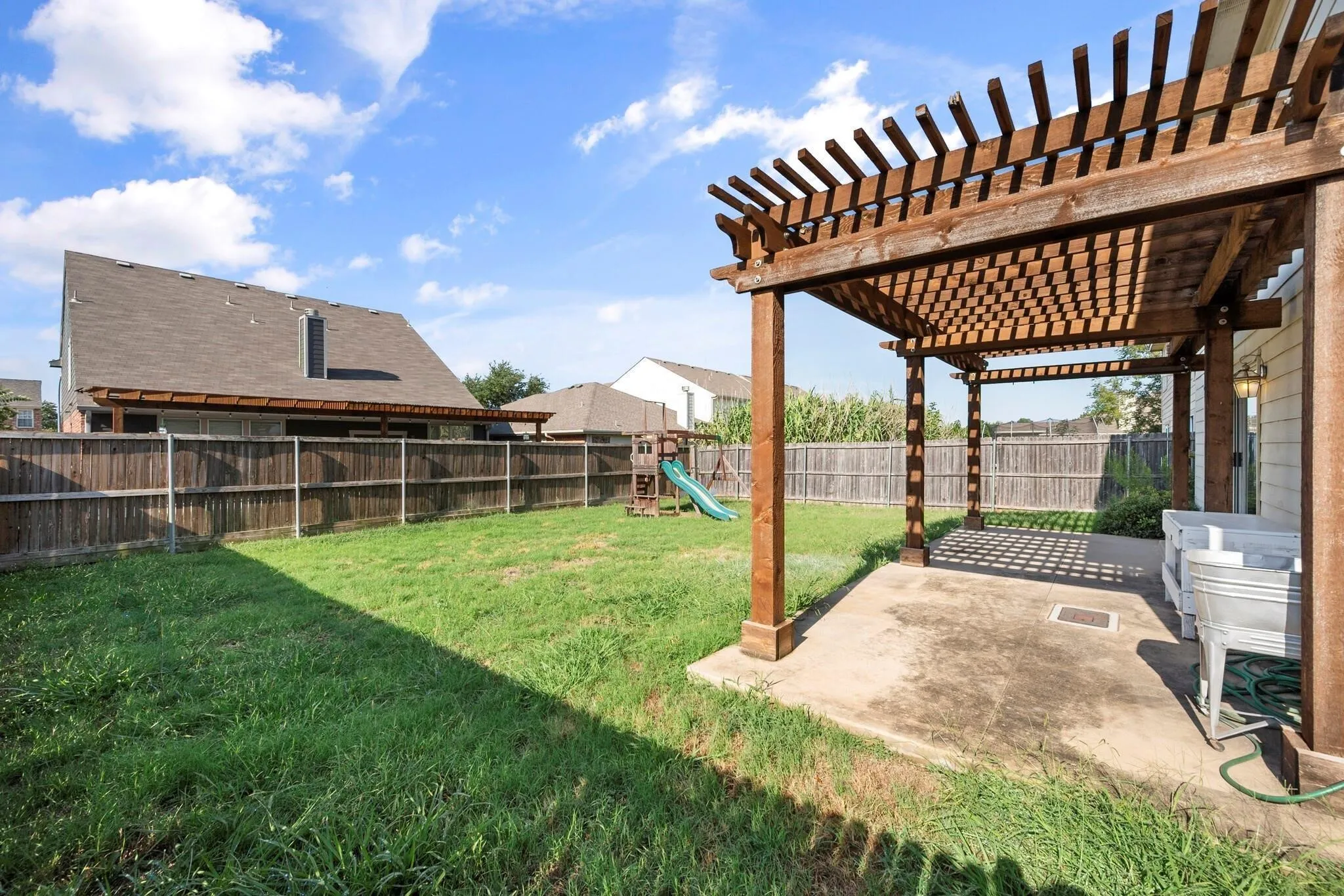 Spacious backyard with a wood pergola, concrete patio, and privacy fencing