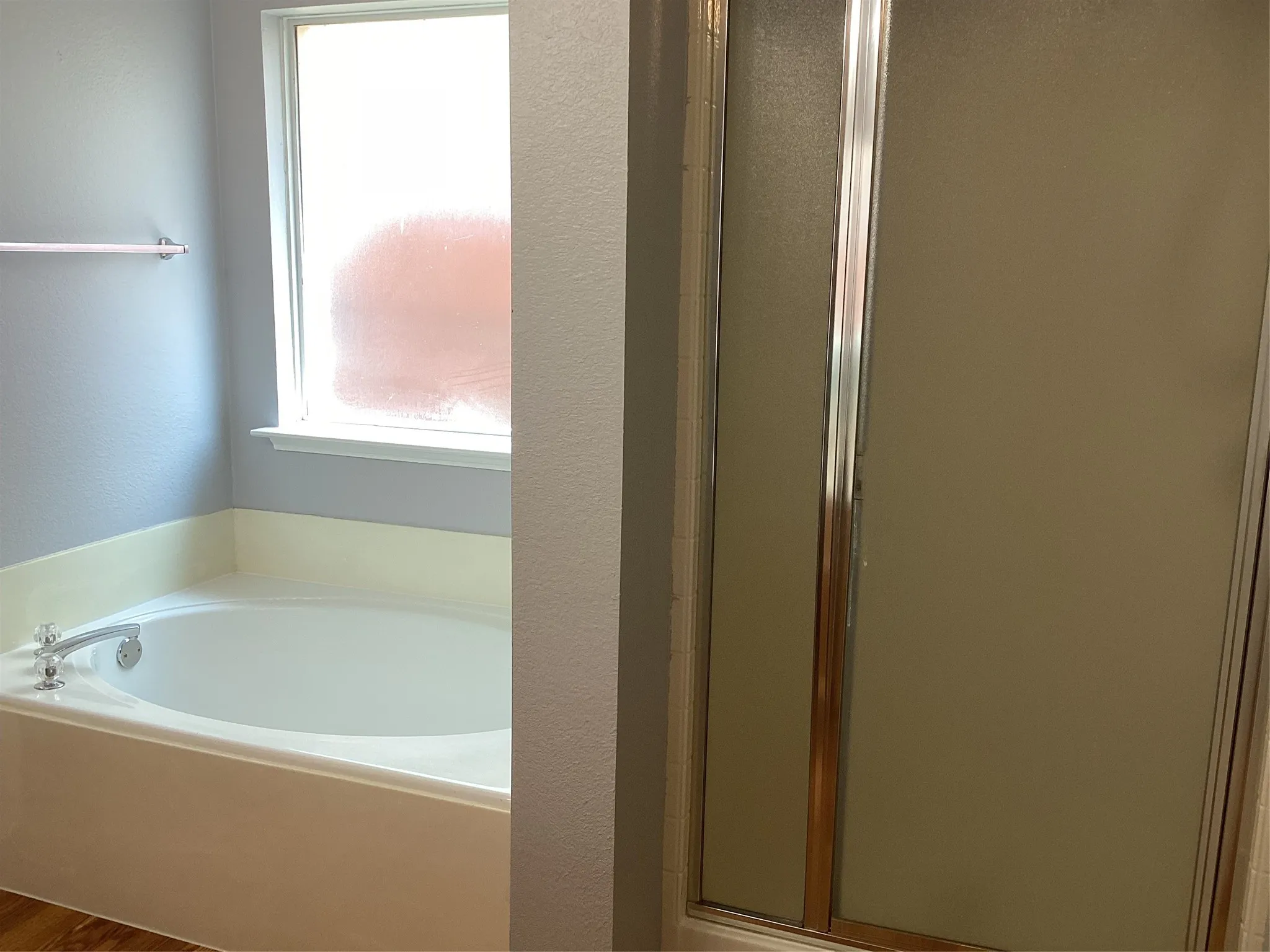 Soaking tub with chrome fixtures, frosted glass window, and an enclosed shower with chrome framing