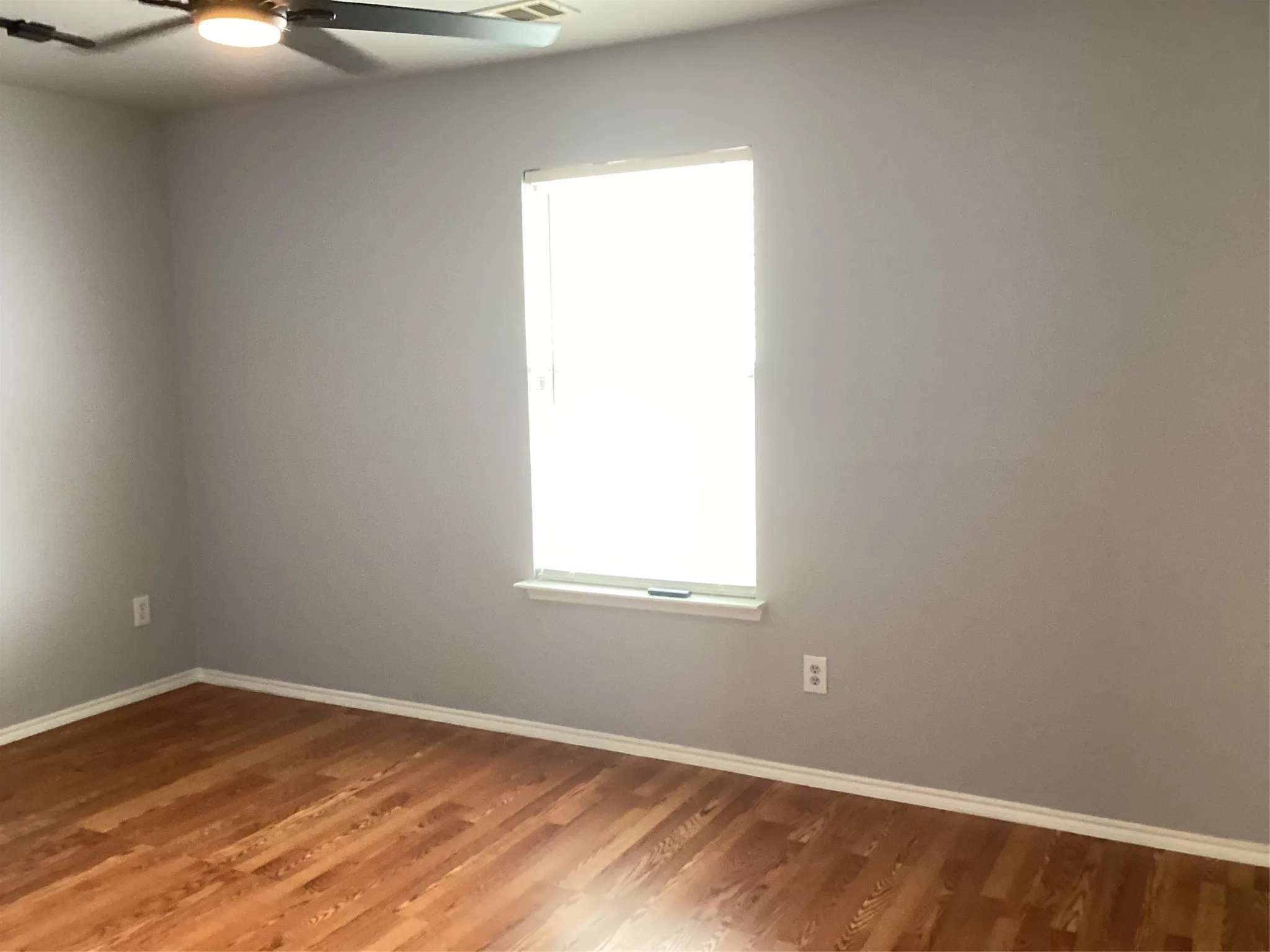 Wood-finish flooring, light gray walls, white trim, and a ceiling fan with integrated lighting