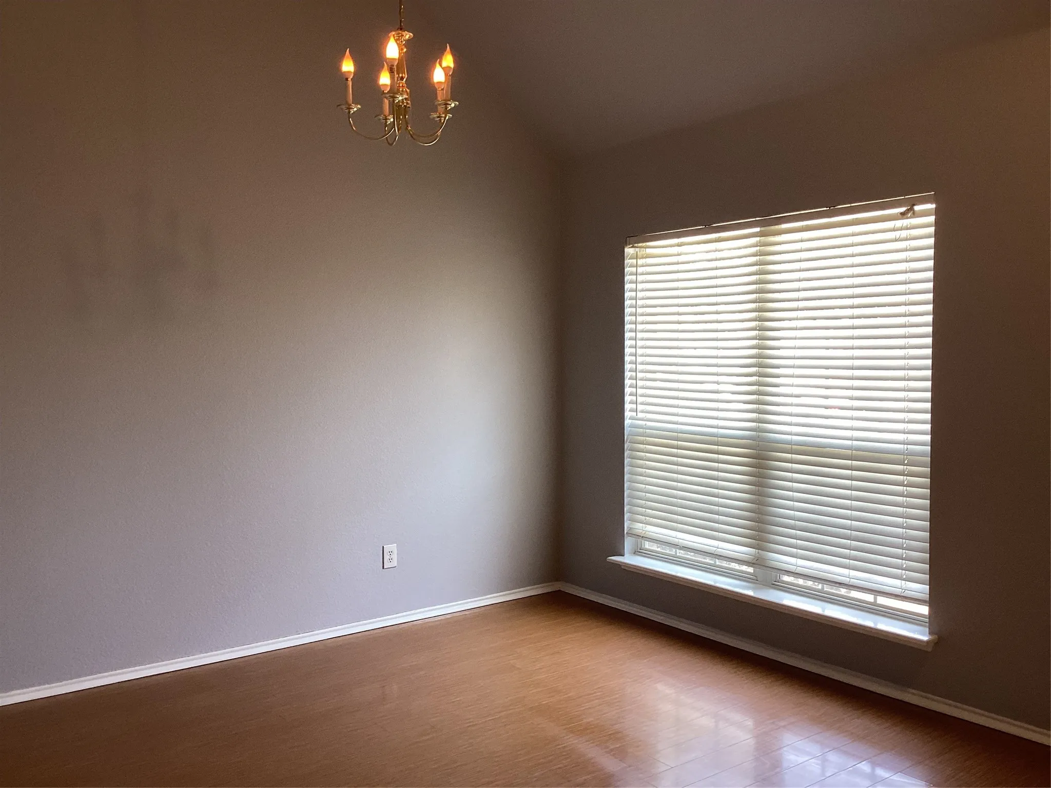 Vaulted ceiling with a brass-finish chandelier, large window with blinds, and wood-finish flooring