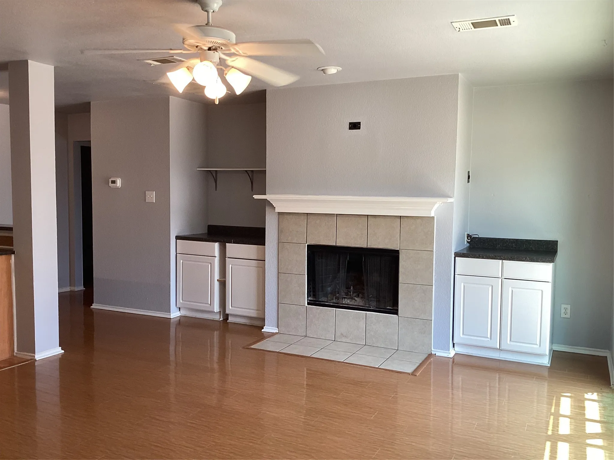 Wood-finish flooring, ceiling fan, recessed lighting, tile-faced fireplace with hearth, and built-in cabinetry with dark countertops