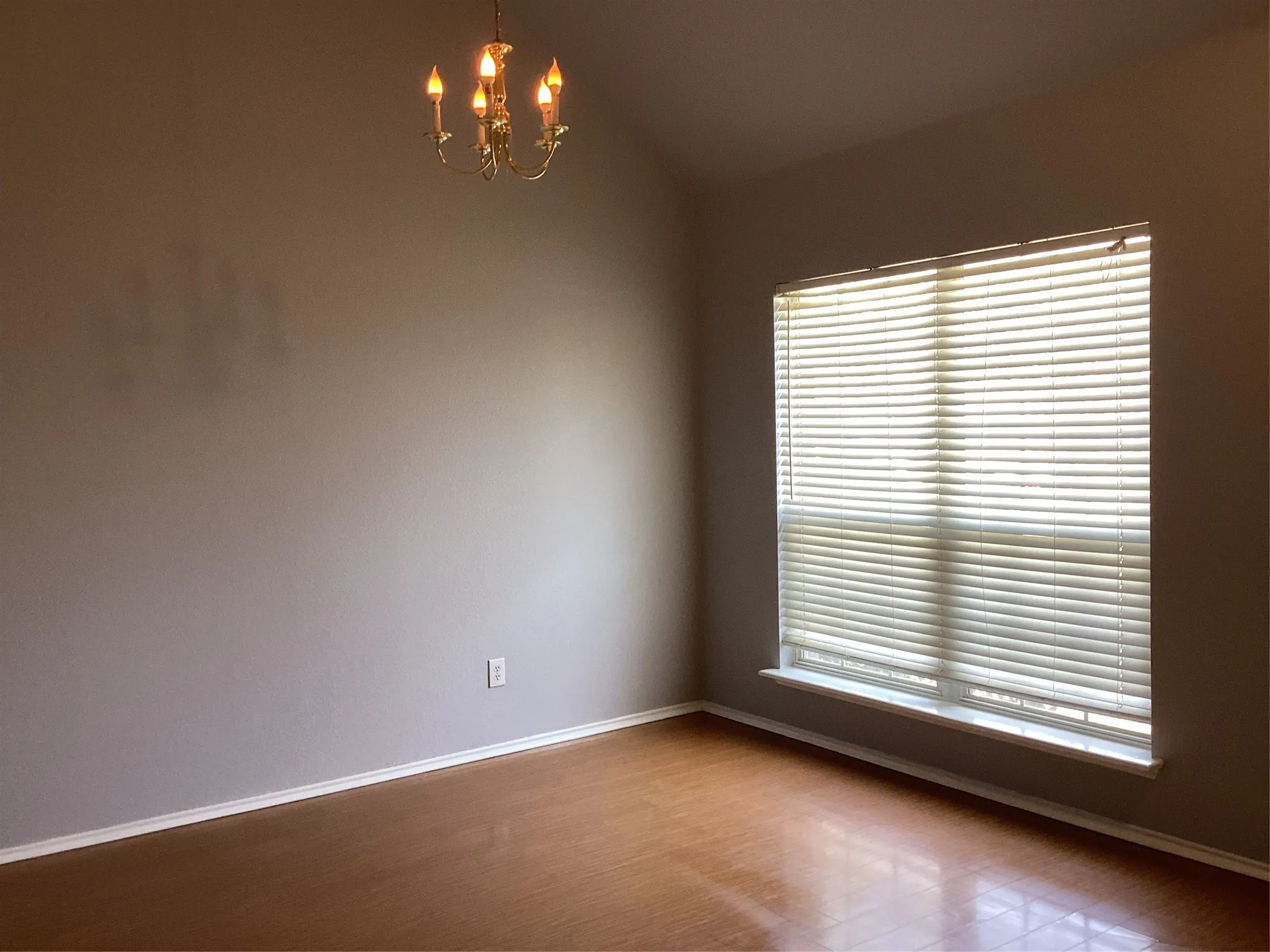 Vaulted ceiling with an antique brass chandelier, large window with blinds, wood-finish flooring, and neutral wall tones