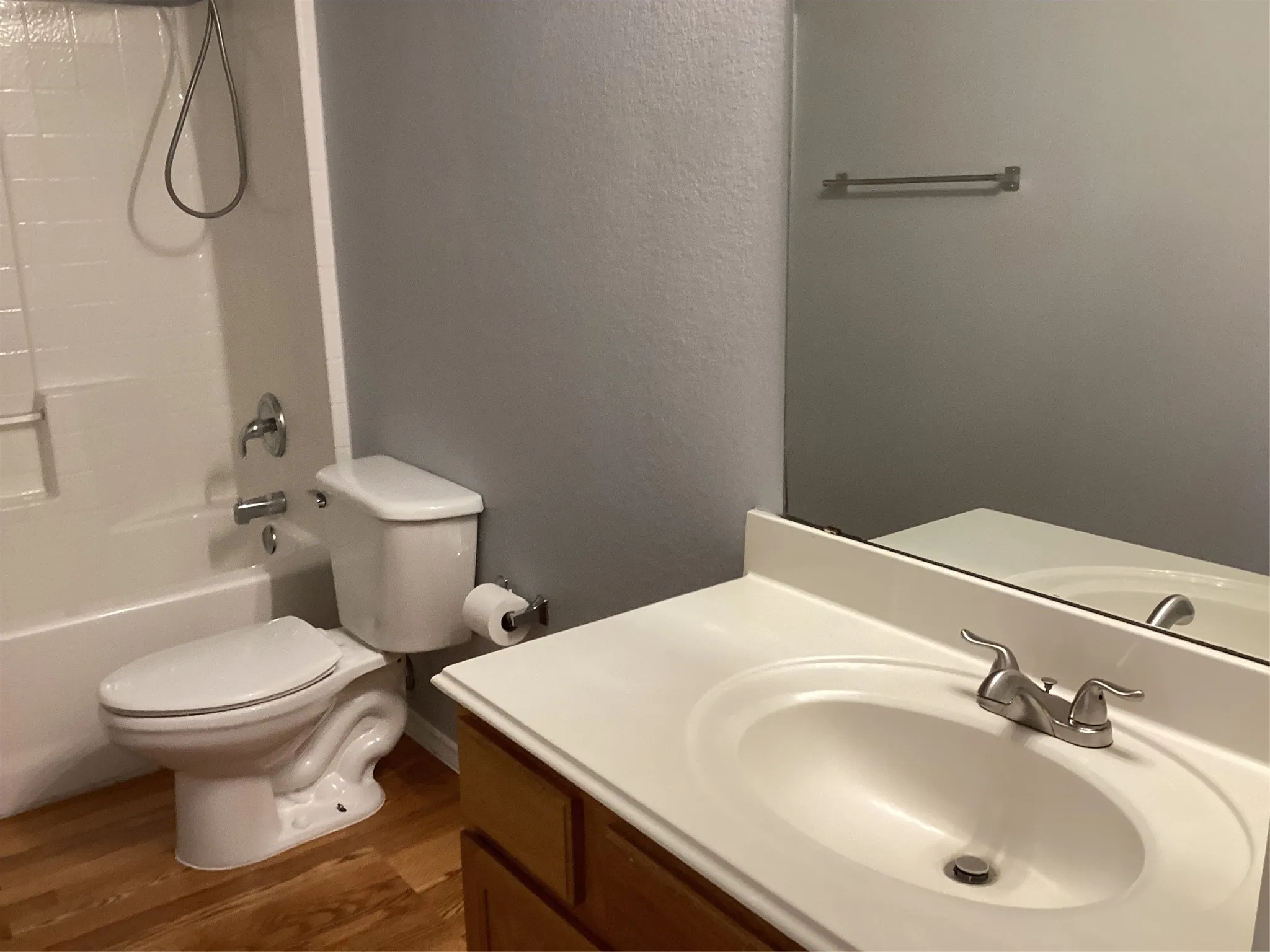 Bathroom featuring a shower-tub combination, single vanity with integrated sink, wood-finish flooring, and a large wall-mounted mirror