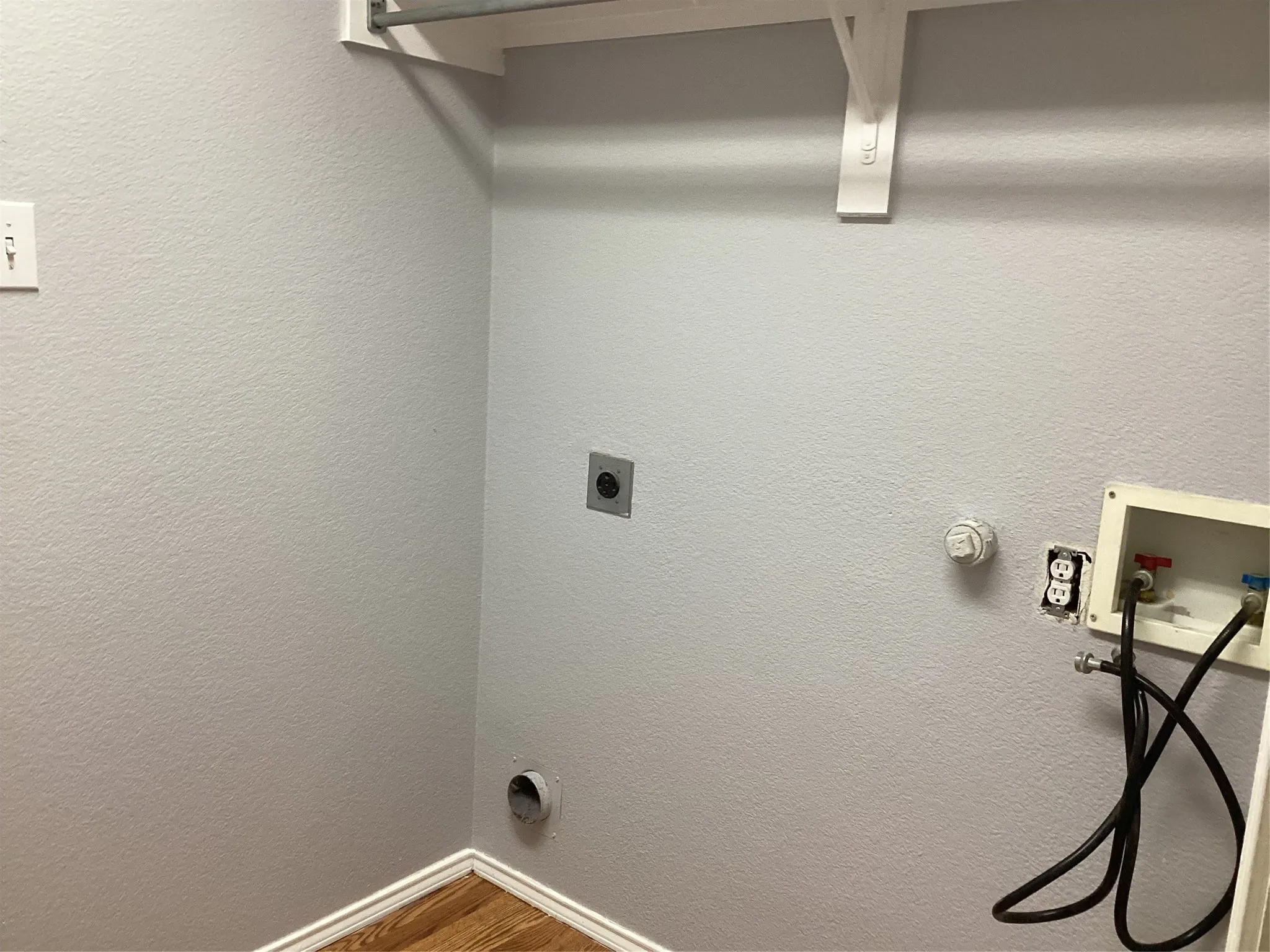 Laundry area with wood-finish flooring, light grey walls, and a white wall-mounted shelf