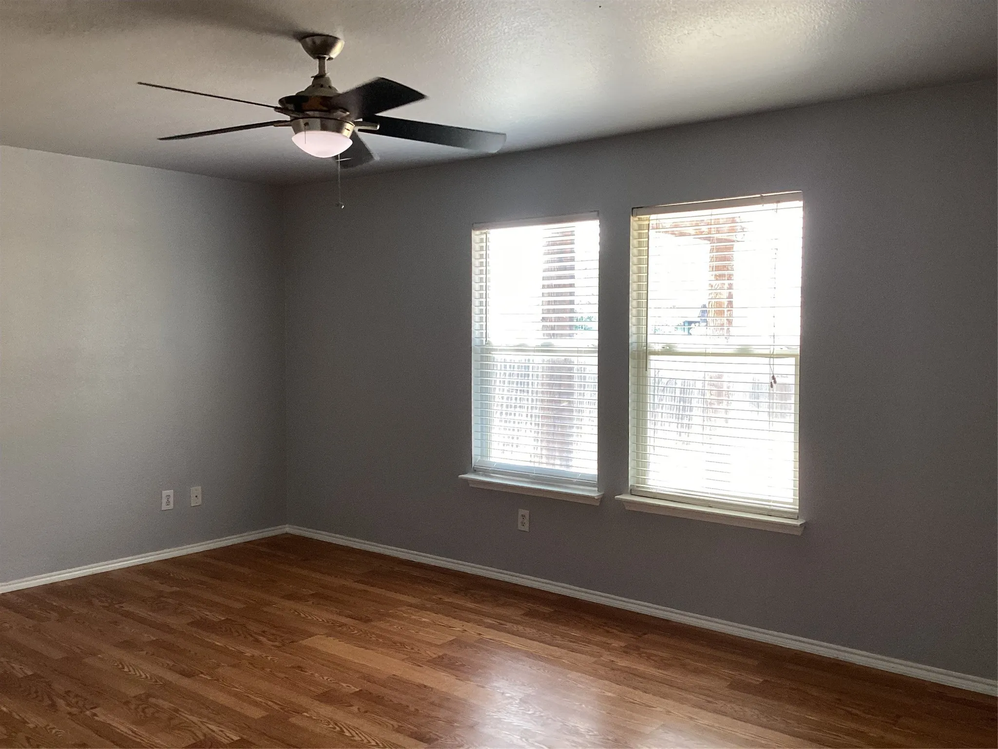 Wood-finish flooring with a neutral wall color, two windows, and a ceiling fan with integrated lighting