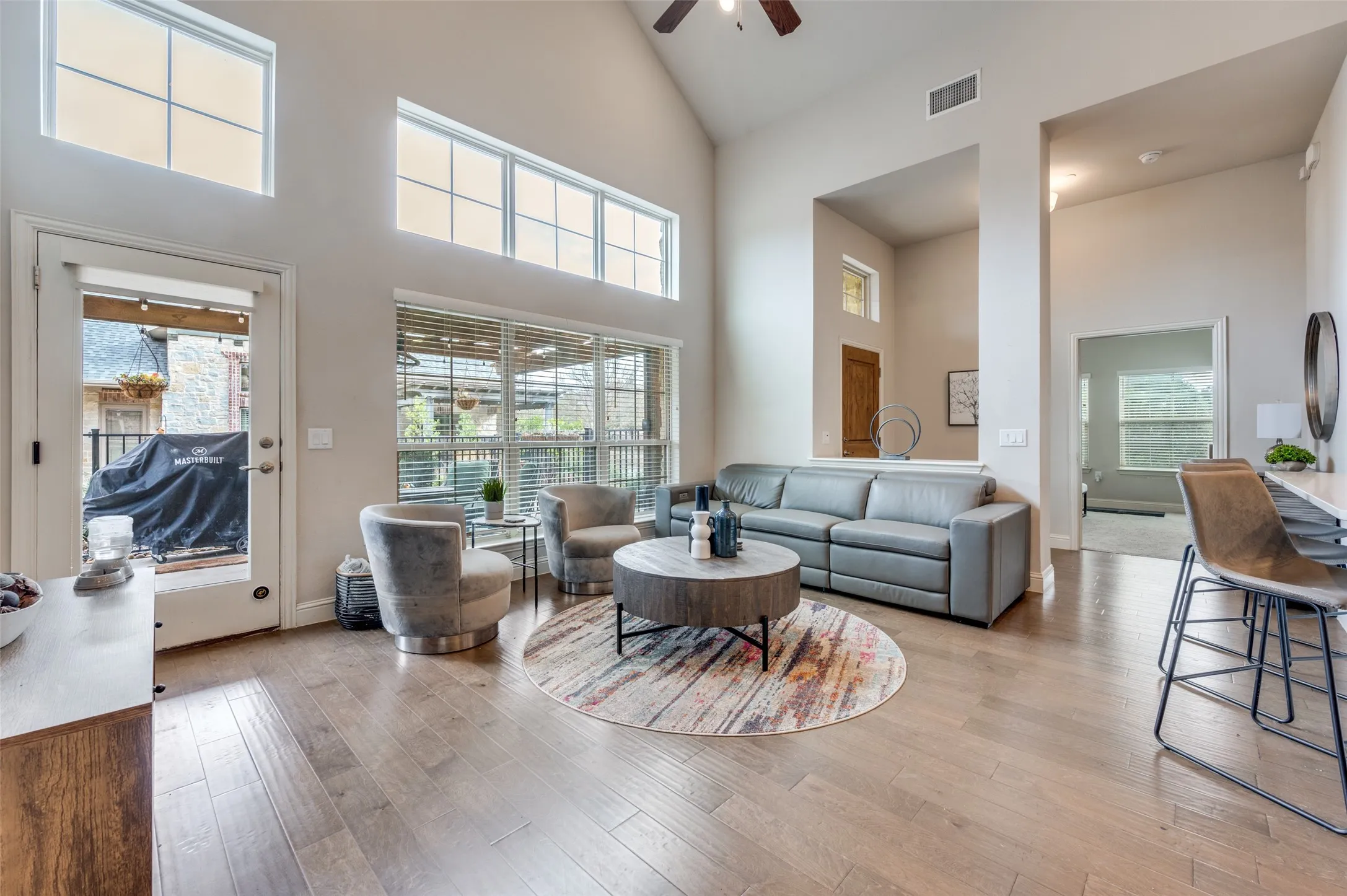 Vaulted ceiling with a ceiling fan, wood-finish flooring, multiple transom windows, and a glass-paneled door opening to an exterior area