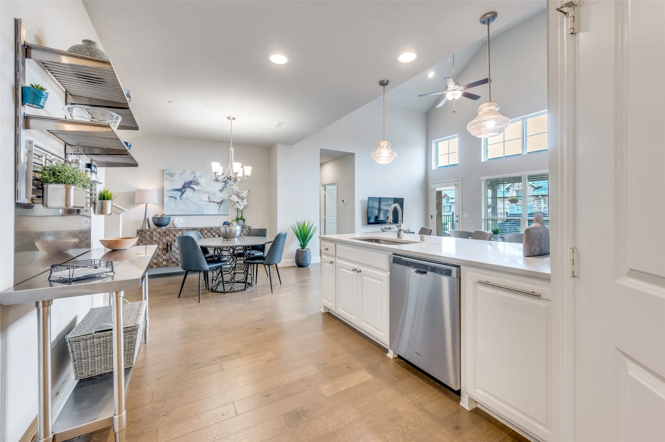 Open-concept living area with wood-finish flooring, white cabinetry, stainless steel appliances, and high ceilings with transom windows