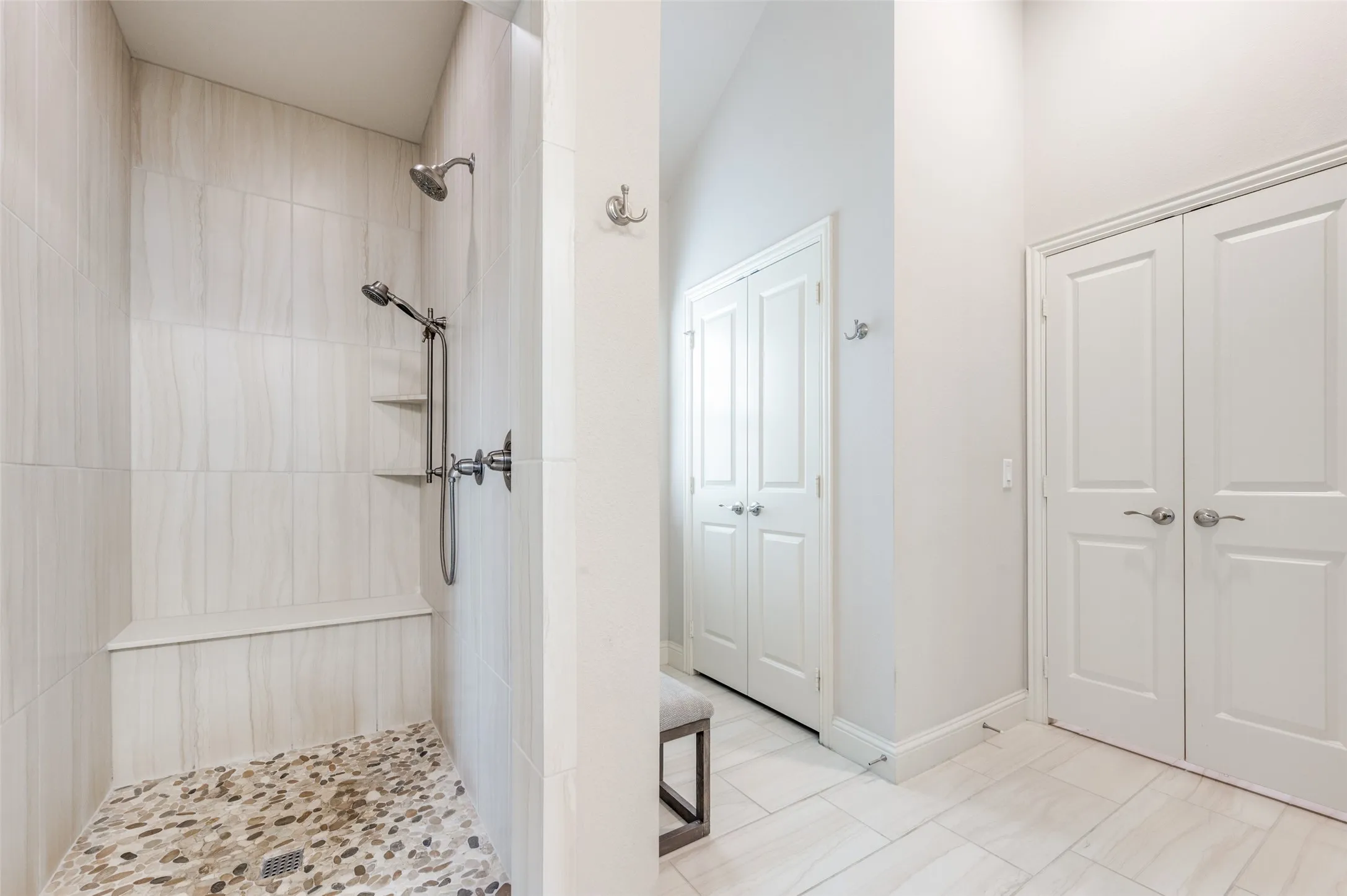 Spacious shower with stone pebble flooring, integrated bench seating, dual shower heads, and built-in shelving