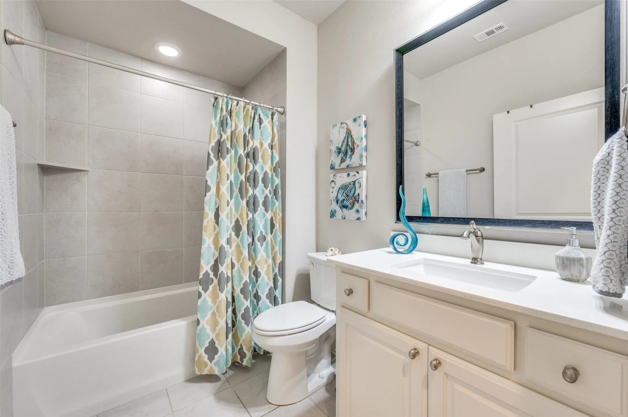 Bathroom featuring a built-in tub with tile surround, recessed shower niche, single-sink vanity with white countertop, and a large framed mirror