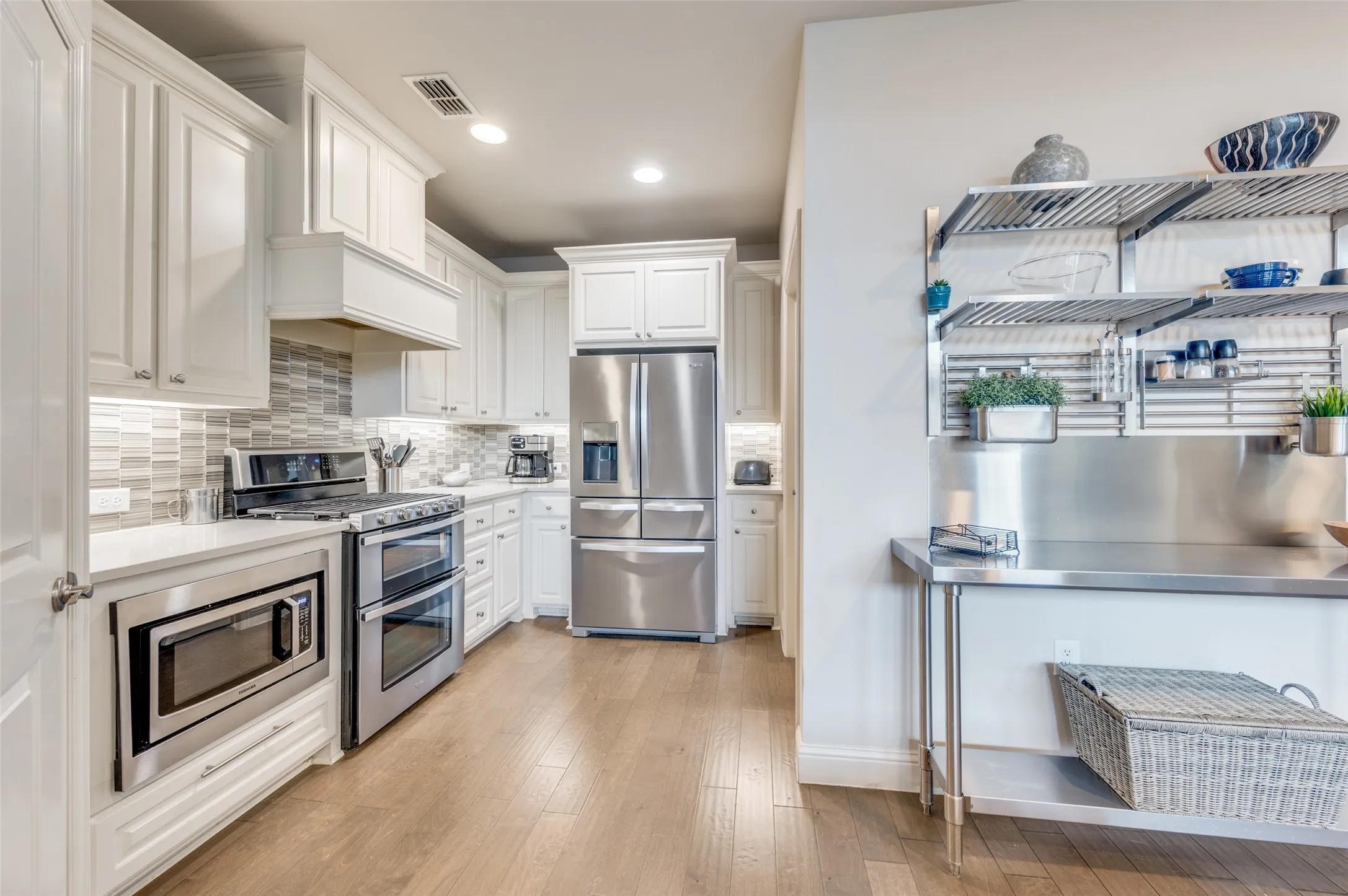 Kitchen featuring white cabinetry, stainless steel appliances, a tile backsplash, light-toned wood-finish flooring, and recessed lighting