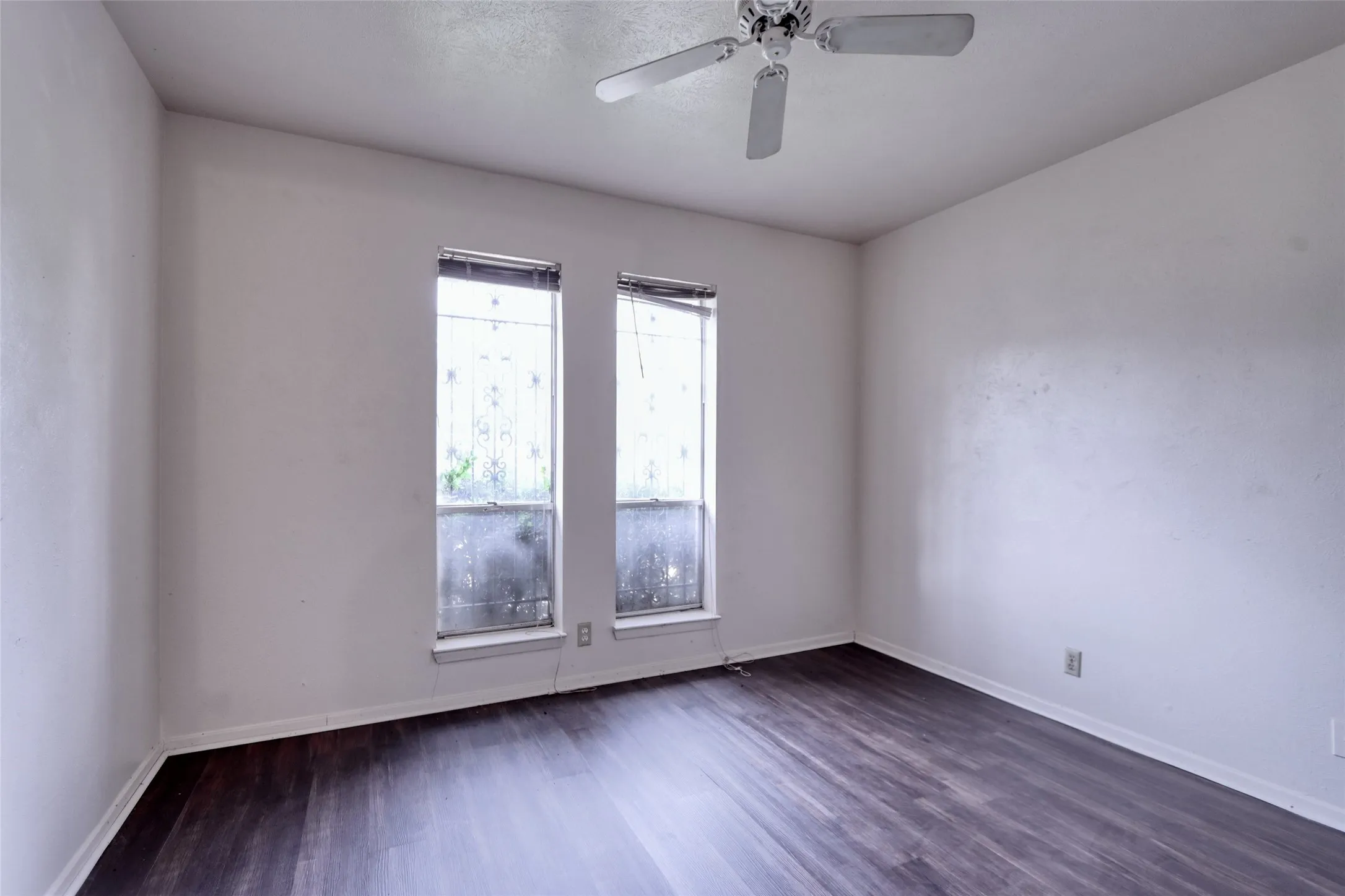 Room featuring wood-finish flooring, white walls, two windows, and a ceiling fan