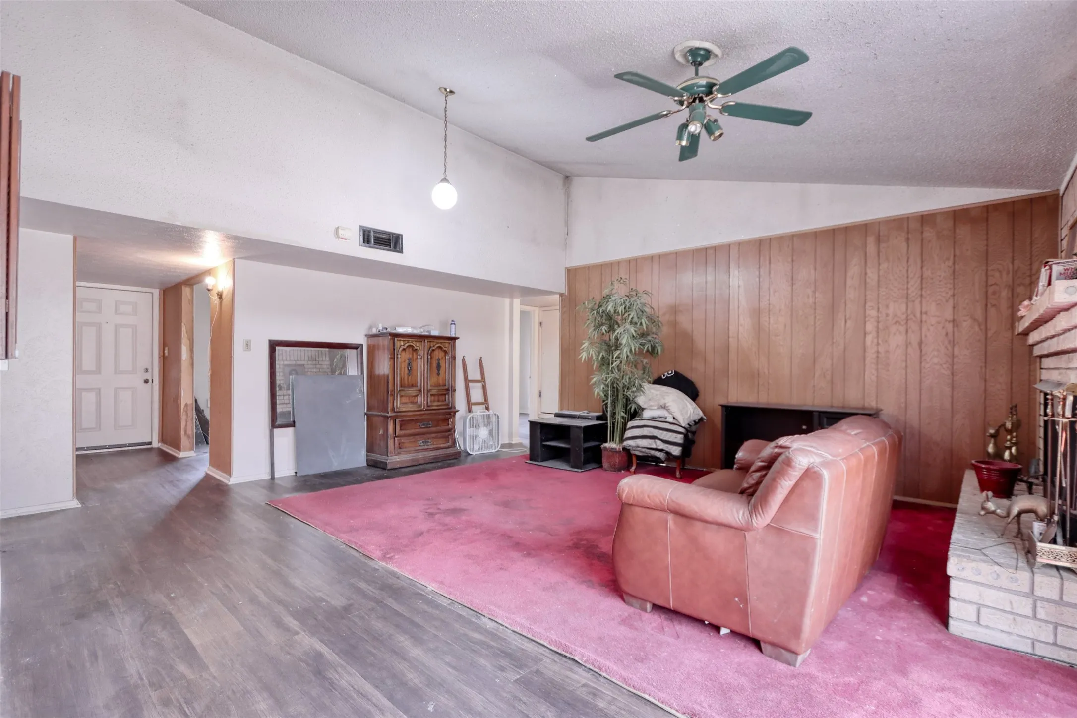 Vaulted ceiling with exposed wood-finish paneling, brick fireplace with a raised hearth, and wood-finish flooring