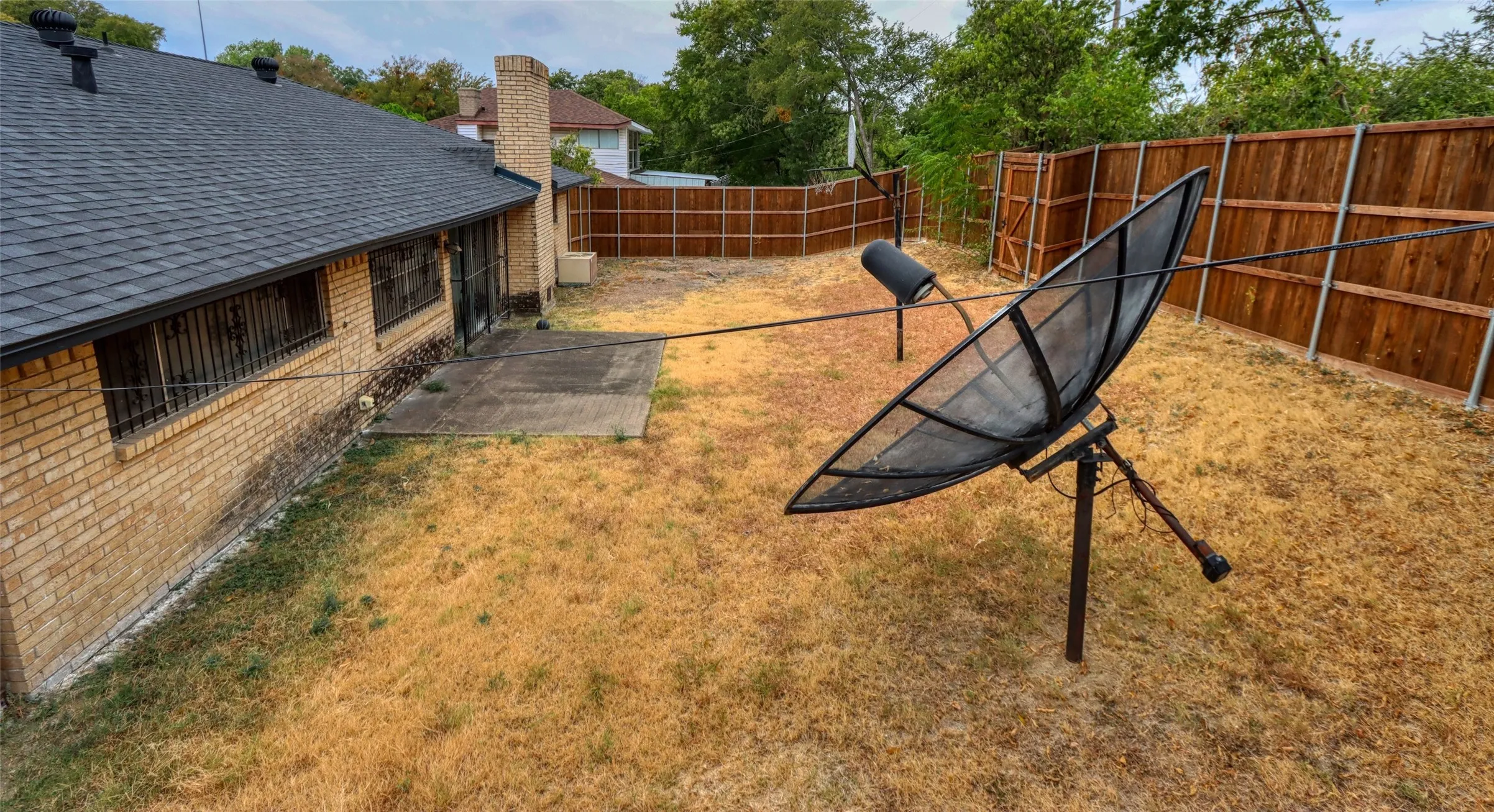 Fenced backyard featuring a brick exterior, concrete patio, and shingle roof