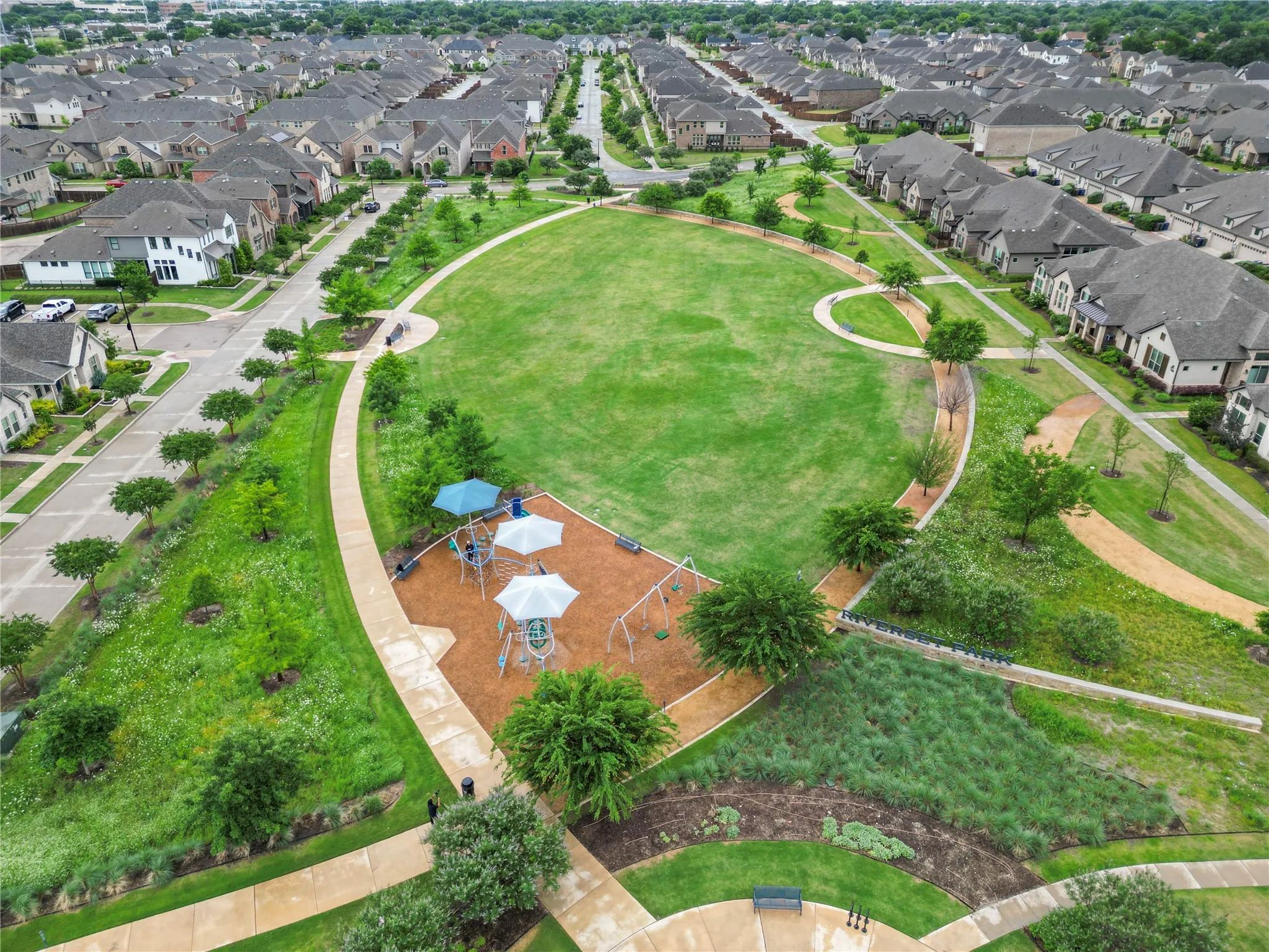 Expansive green space featuring a playground with shade structures, paved walking paths, and mature landscaping