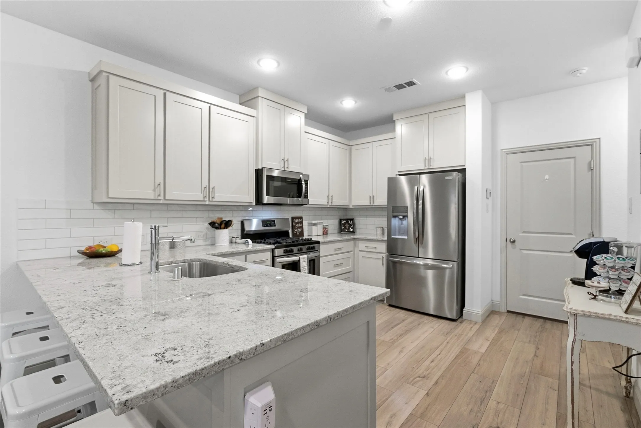 Kitchen featuring light-toned cabinetry, stainless steel appliances, a subway tile backsplash, and light granite countertops