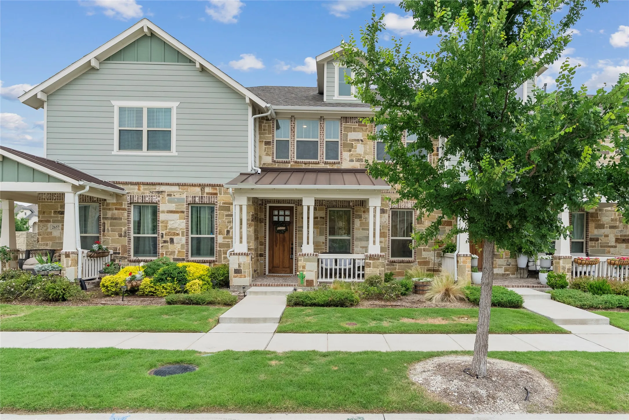 Stone and siding exterior with a covered porch, wood-paneled front door, and mature landscaping