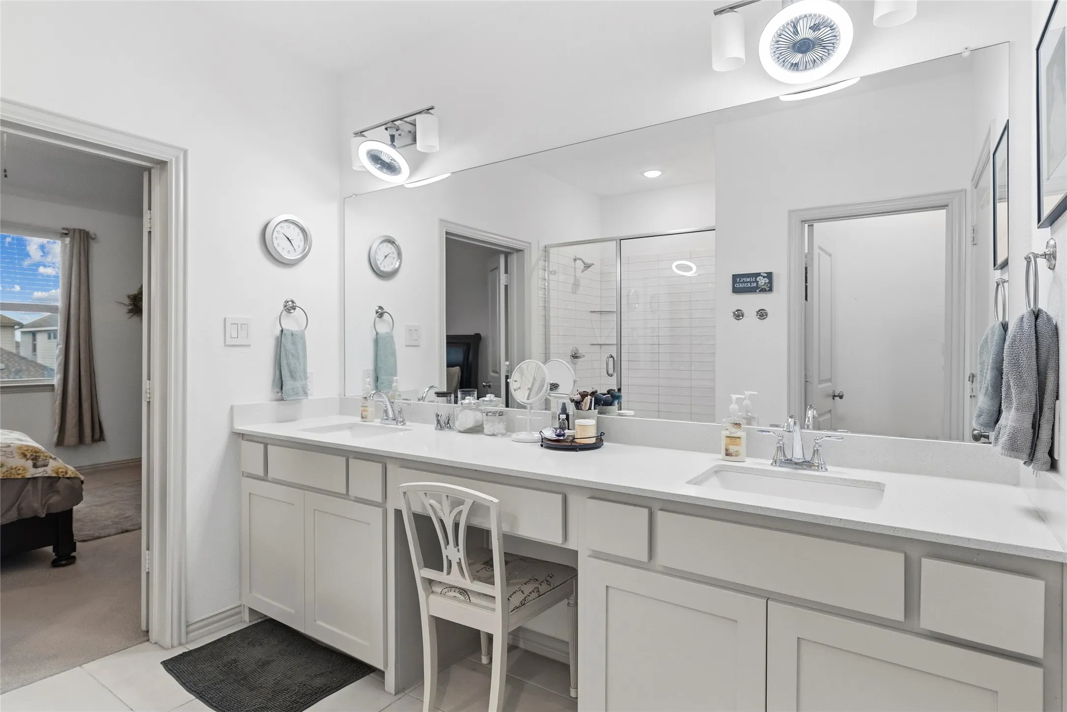 Dual vanities with undermount sinks, expansive countertop, large mirror, and separate shower with glass enclosure