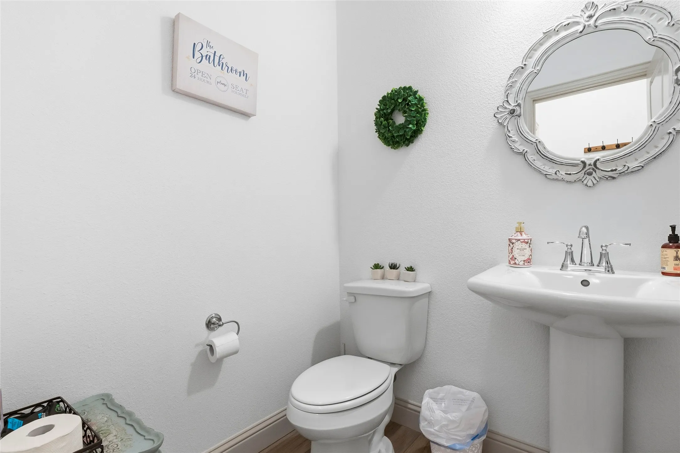 Pedestal sink with chrome faucet, white toilet, and wood-finish flooring