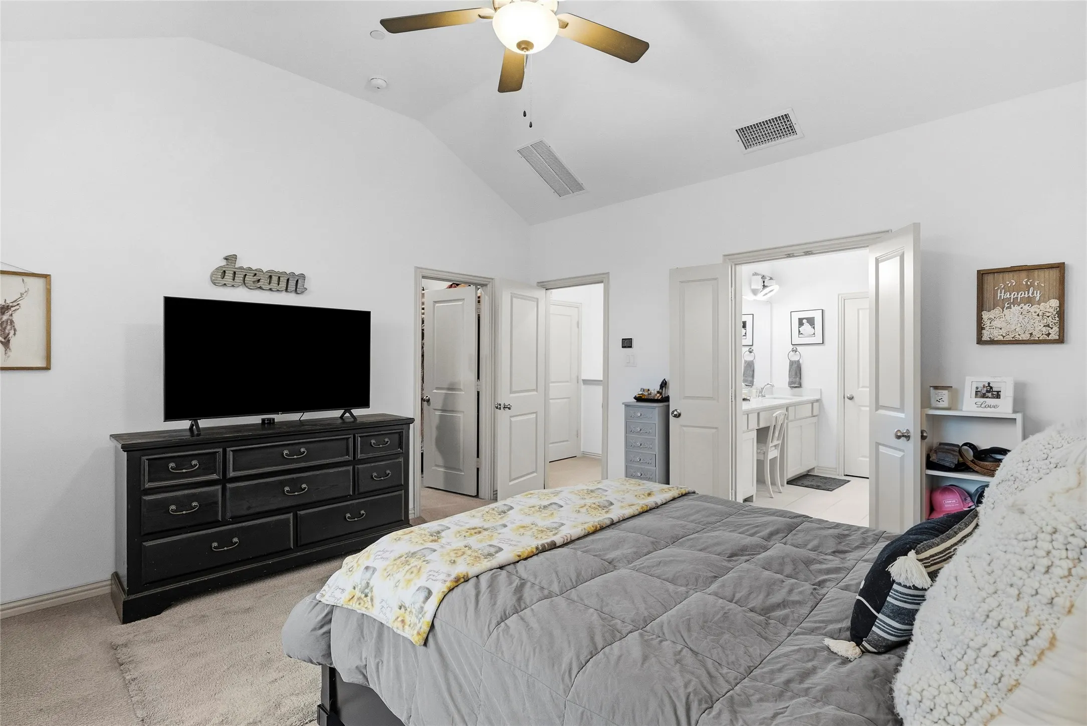 Vaulted ceiling with a ceiling fan, carpeted flooring, and a bright bathroom with a vanity