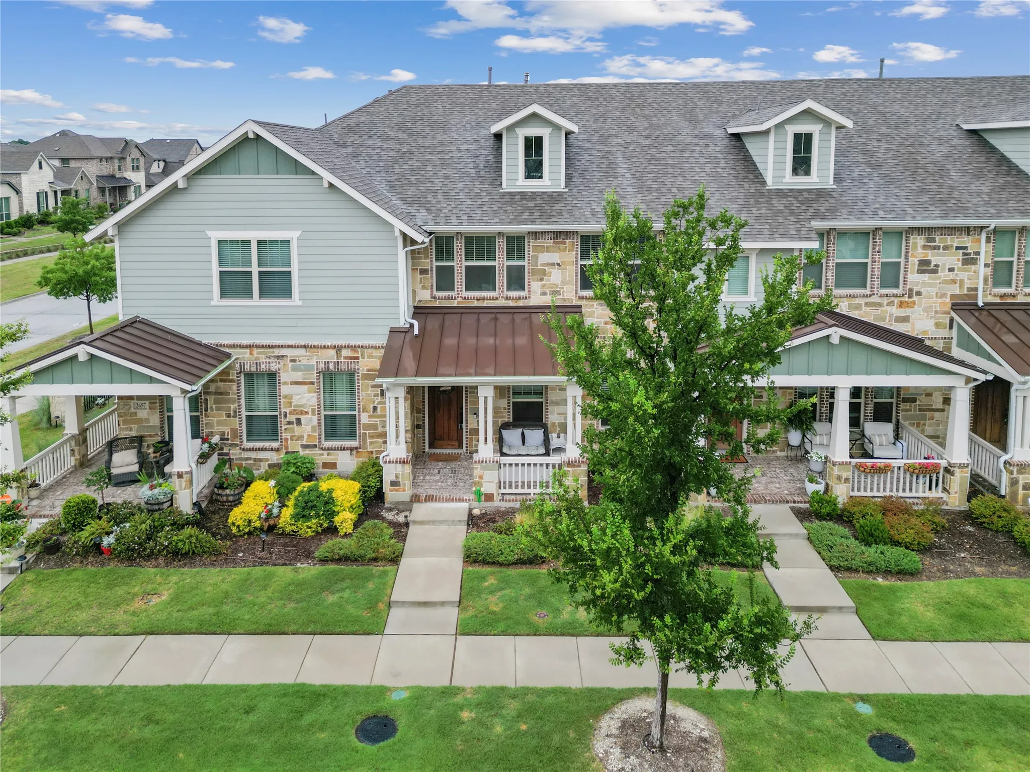 Stone and siding exterior with gabled roof dormers, covered front porches, and manicured landscaping