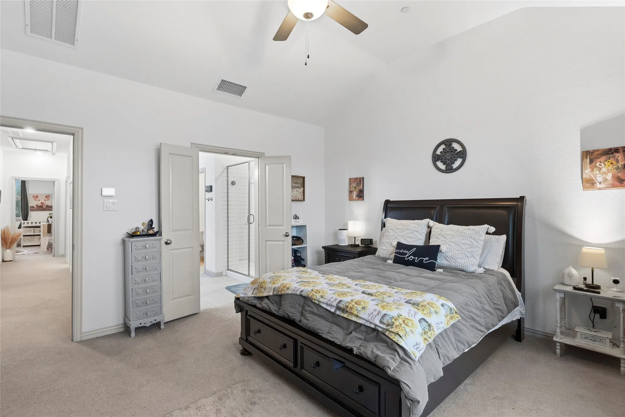 Vaulted ceiling with a ceiling fan, carpeted flooring, and double doors opening to a bathroom with a glass-enclosed shower