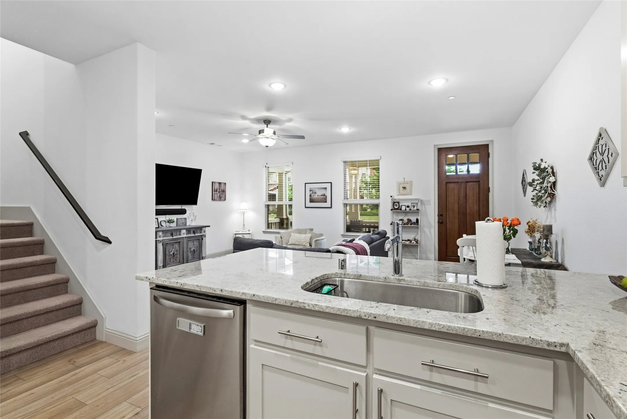 Granite countertops with an undermount sink, stainless steel dishwasher, wood-finish flooring, a wood paneled door with window inserts, and white cabinetry