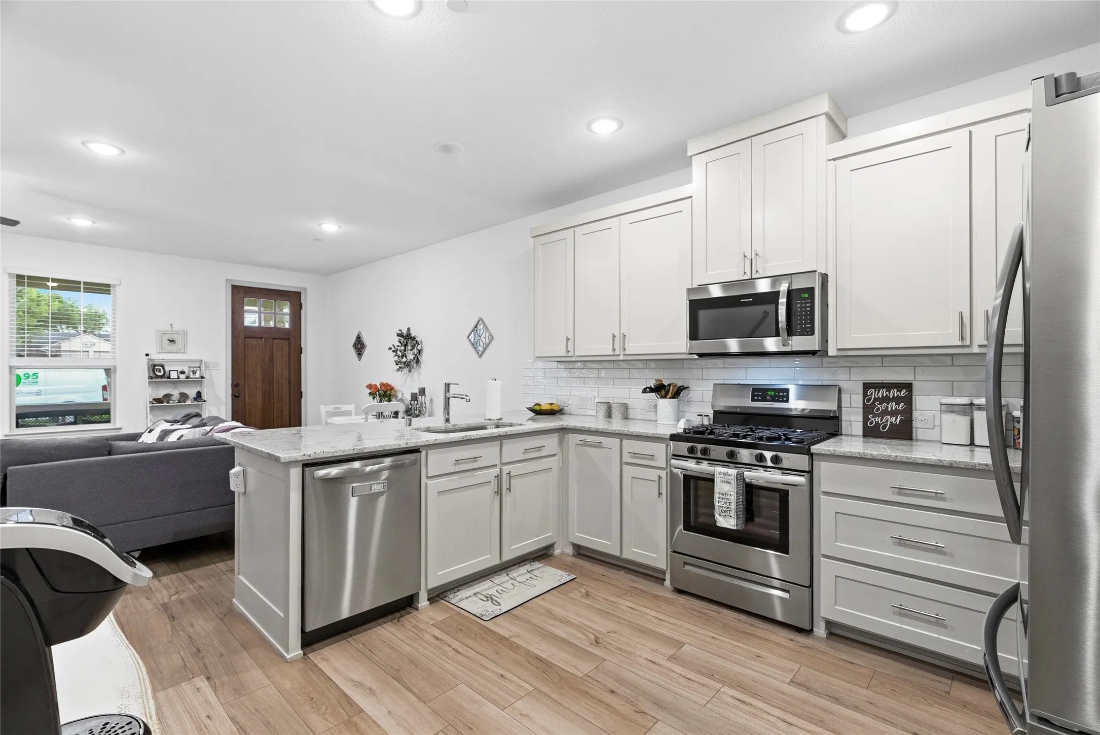 Kitchen featuring an island with a built-in sink, stainless steel appliances, white cabinetry, light-toned wood-finish flooring, and recessed lighting