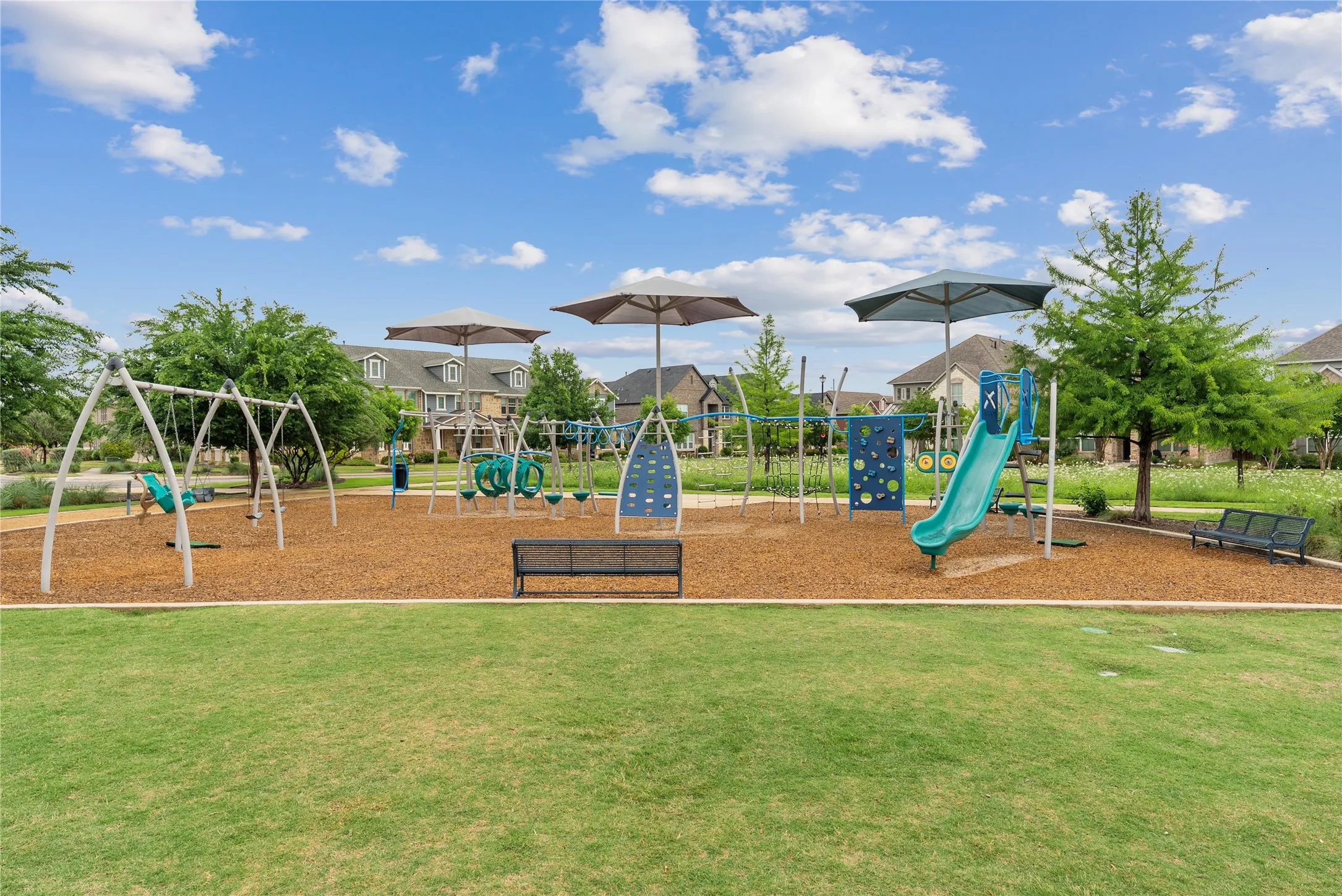 Community playground featuring multiple swing sets, a slide, climbing structures, and shaded seating areas