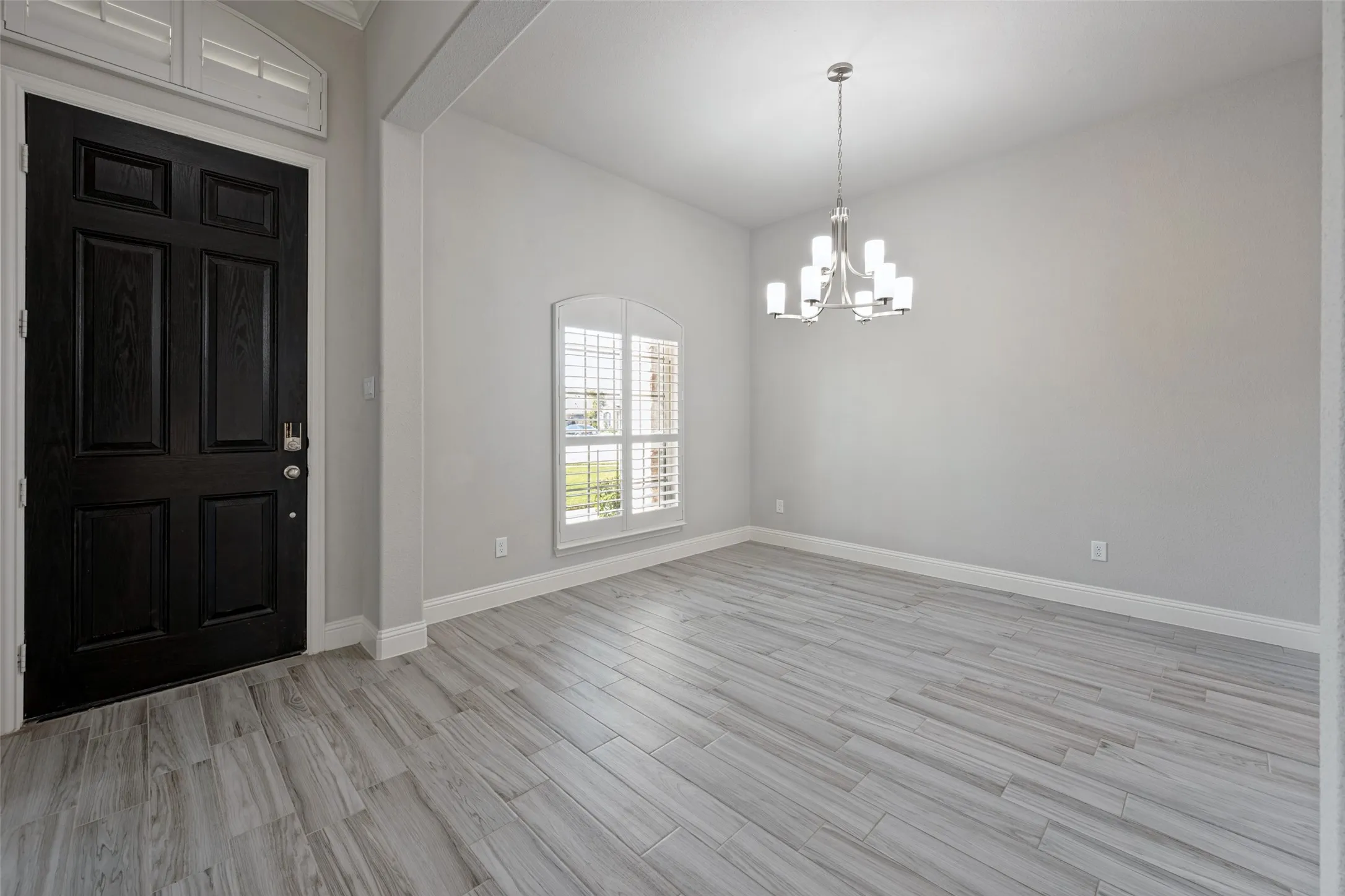 Wood-look tile flooring, arched window with plantation shutters, contemporary chandelier, and a paneled entry door with transom window
