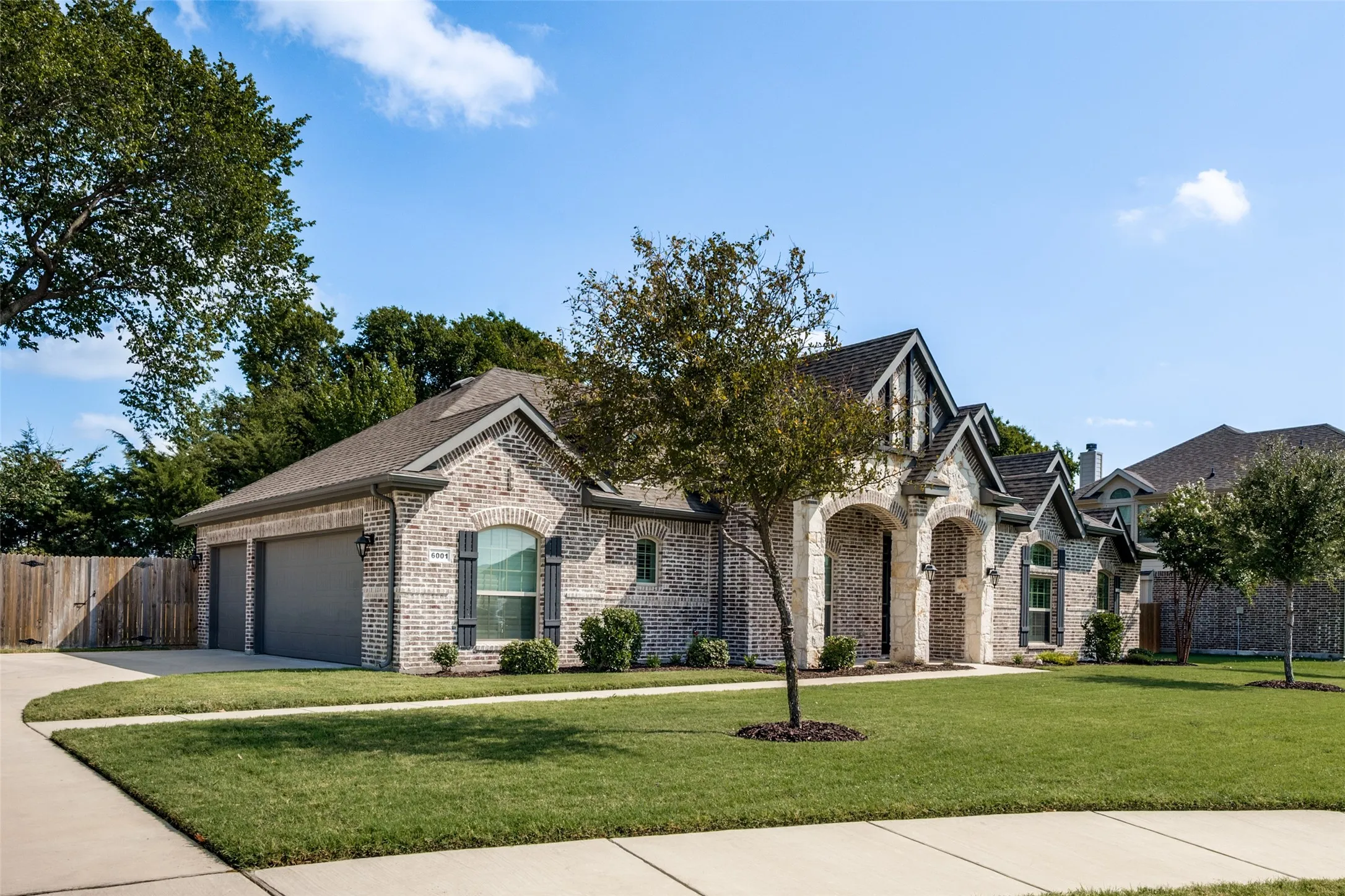 Brick and stone exterior with arched entryway, dark shingles, side entry three-car garage and manicured lawn.