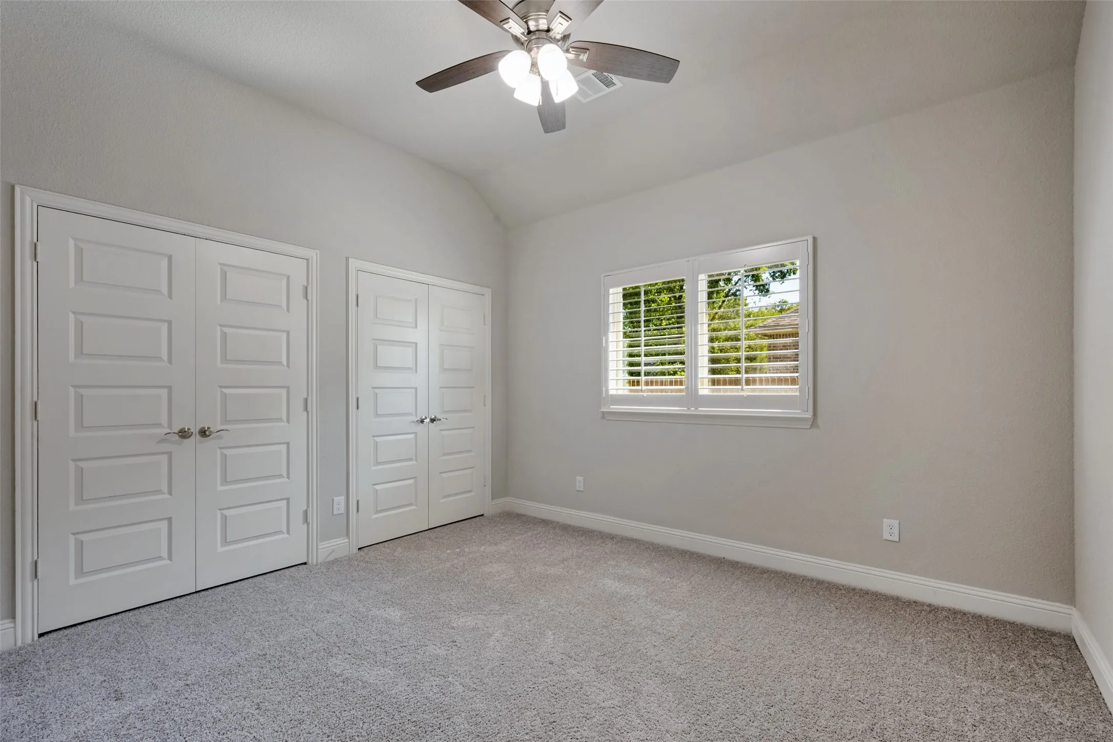 Carpeted bedroom featuring a ceiling fan, a window with plantation shutters and spacious connecting closets.
