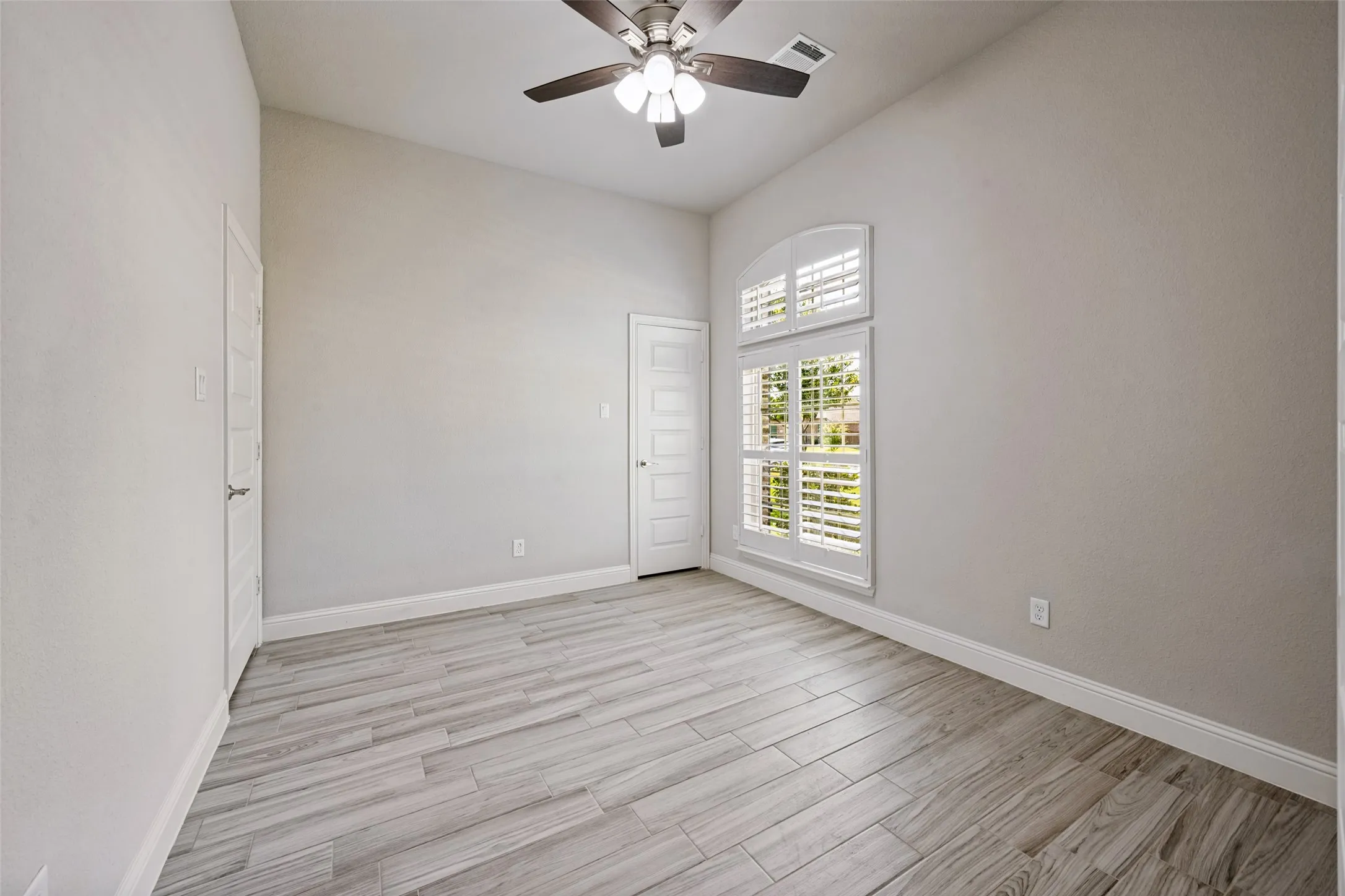 The office features a tall ceiling with a ceiling fan, light gray walls, wood-look tile flooring and a window with plantation shutters. Also feautured is a walk-in closet to store your supplies or turn it into a 5th bedroom.