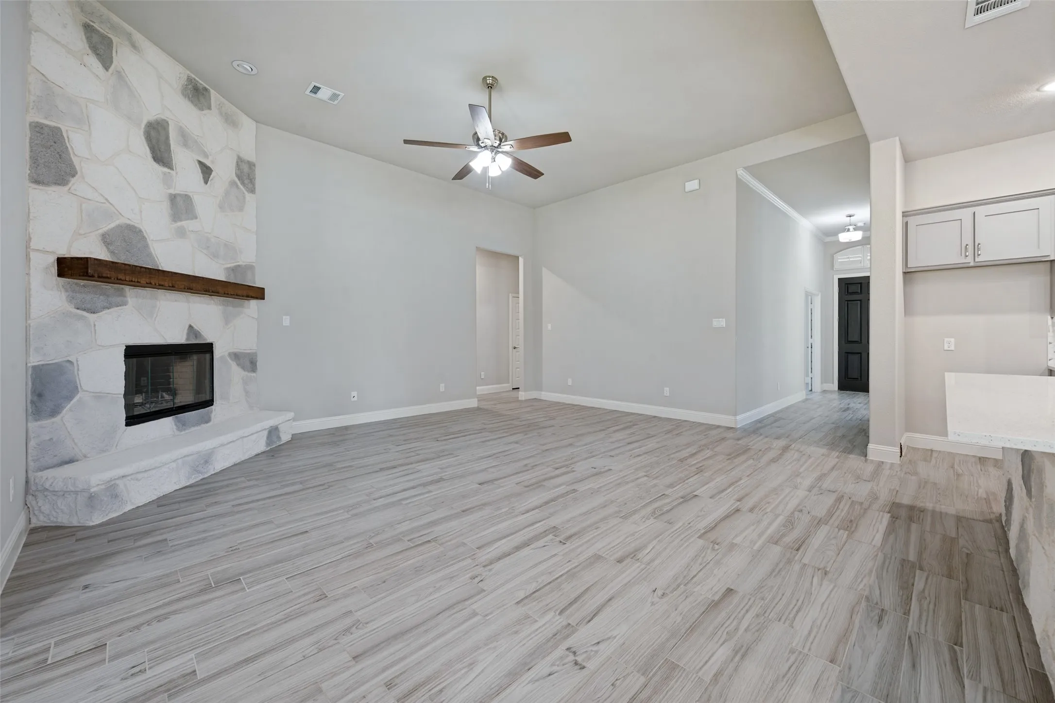 Spacious living area featuring a blown in stone facade fireplace with a wood mantel, light-toned wood-look tile flooring and a ceiling fan and light which are controled with a remote.