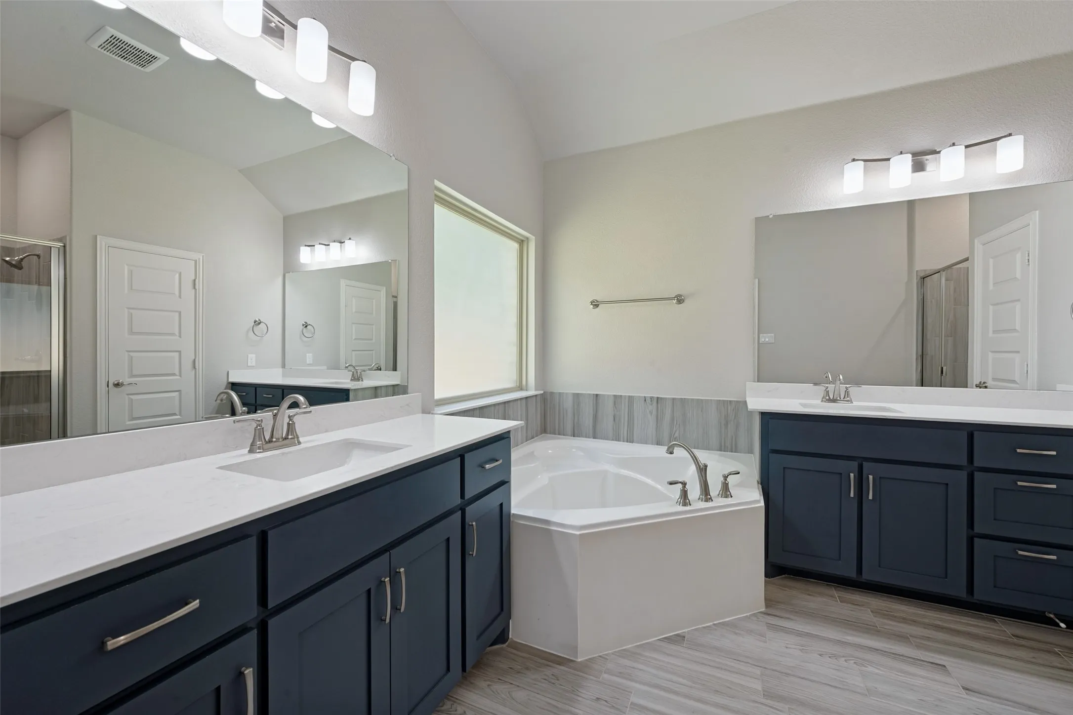 Dual vanities with white countertops, deep blue cabinetry, corner soaking tub, and wood-look tile flooring grace the ensuite bathroom. And look at the drawer space!