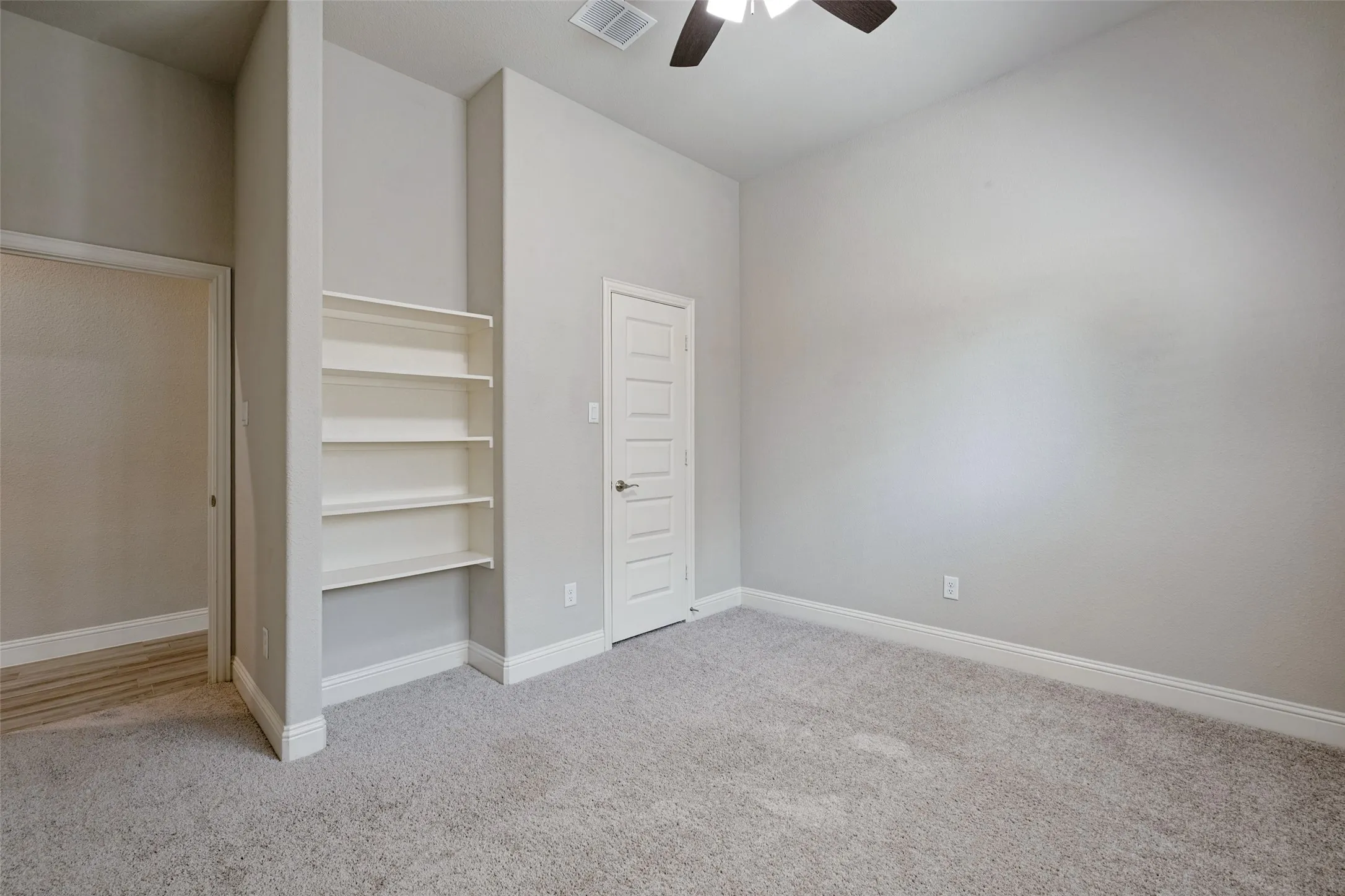 This secondary bedroom features built-in shelving and a walk in closet as well as a ceiling fan.