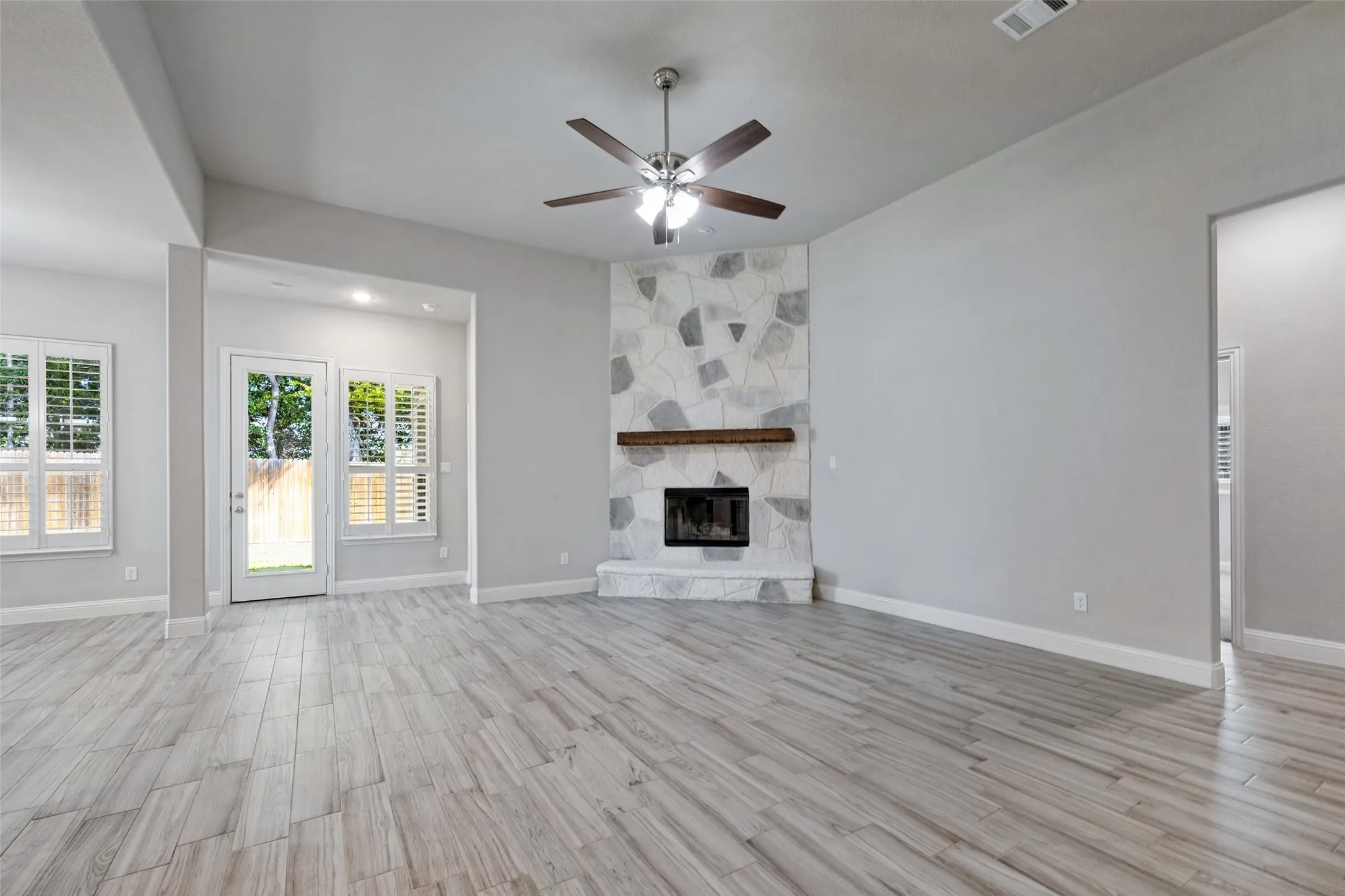 Vaulted ceiling with a ceiling fan, fireplace with hearth, and white plantation shutters on windows. This door leads you out to the spacious covered porch.