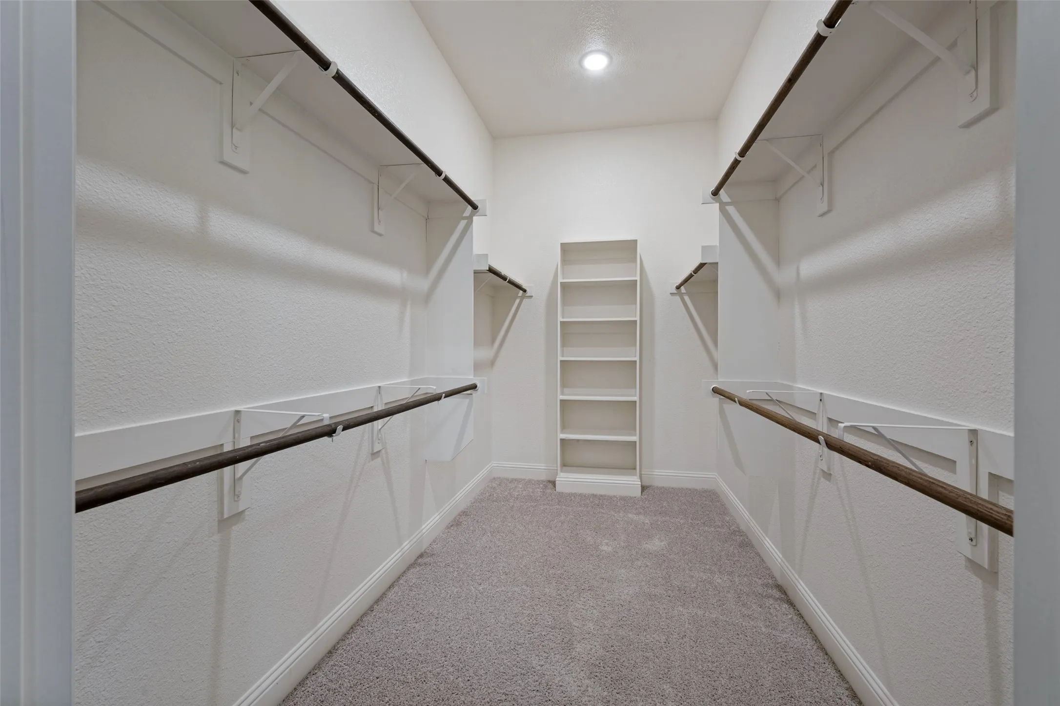 Walk-in closet with carpet flooring, built-in shelving, white walls and hanging space for your long items of clothing.