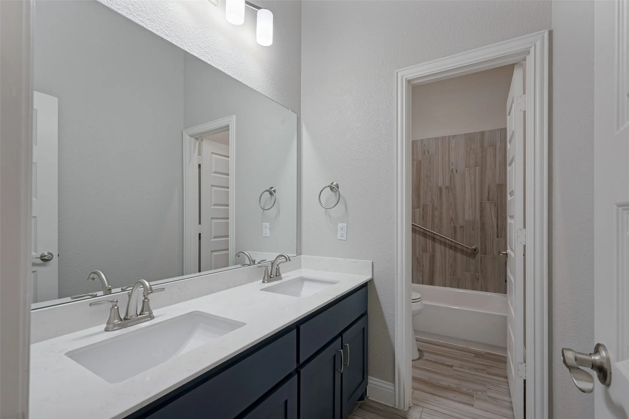 The hall bath features dual undermount sinks with brushed nickel faucets, non-natural quartz-finish countertop, oversized wall mirror and tile flooring. The private bathing area features a grab bar and and pull down seat.
