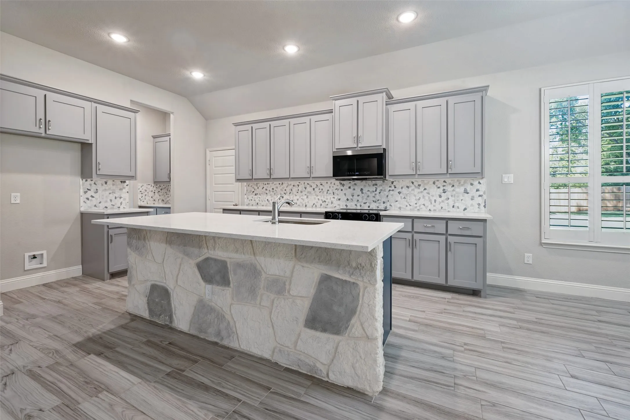 Kitchen featuring a blown in stone facade on the island with a quartz countertop, integrated appliances, and wood-look tile flooring. Of special intrest is the flex oven which converts to a double oven.