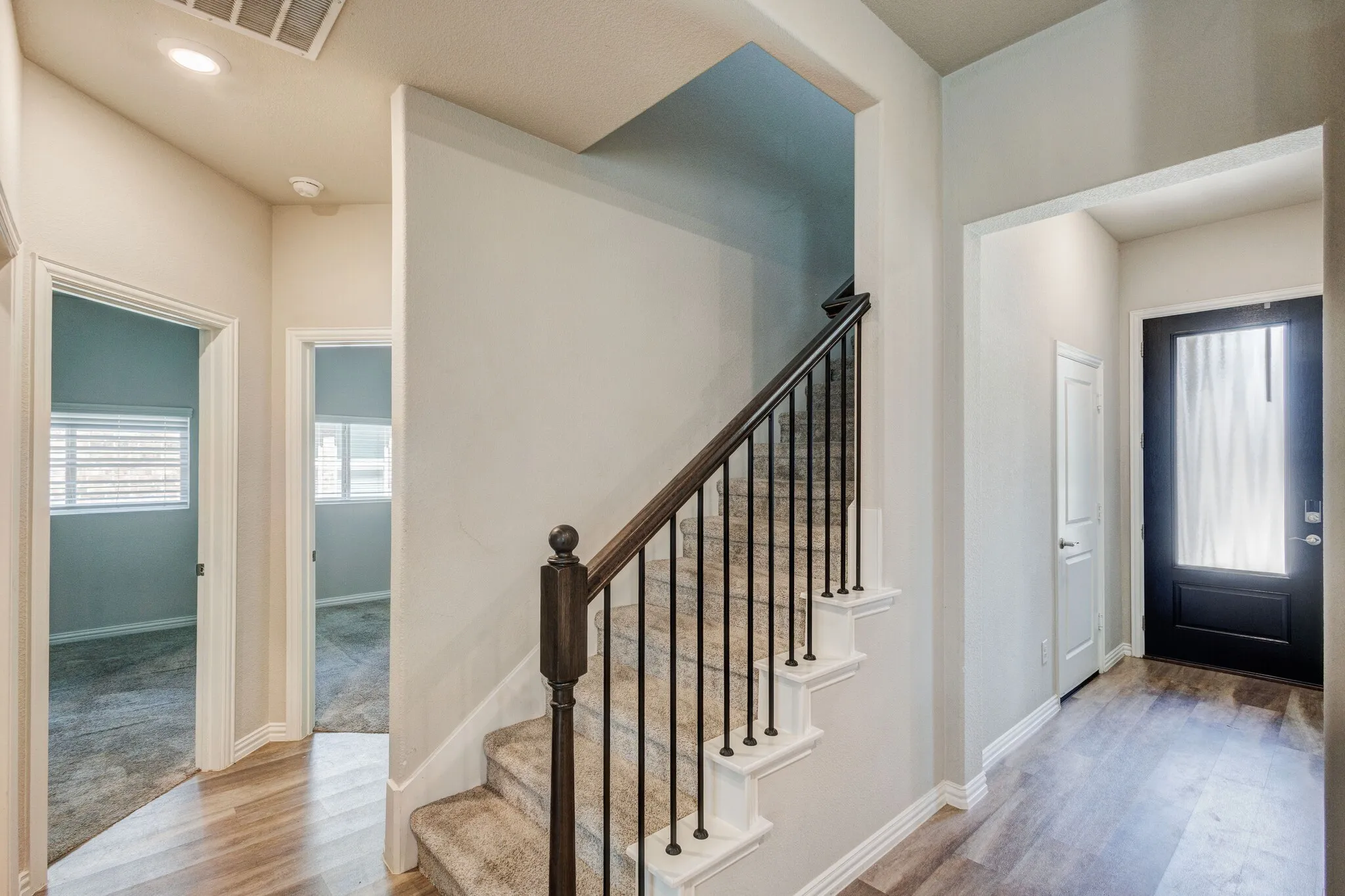 Wood-finish flooring, staircase with wrought iron balusters and dark wood handrail, recessed lighting, and a front entry door with a frosted glass insert