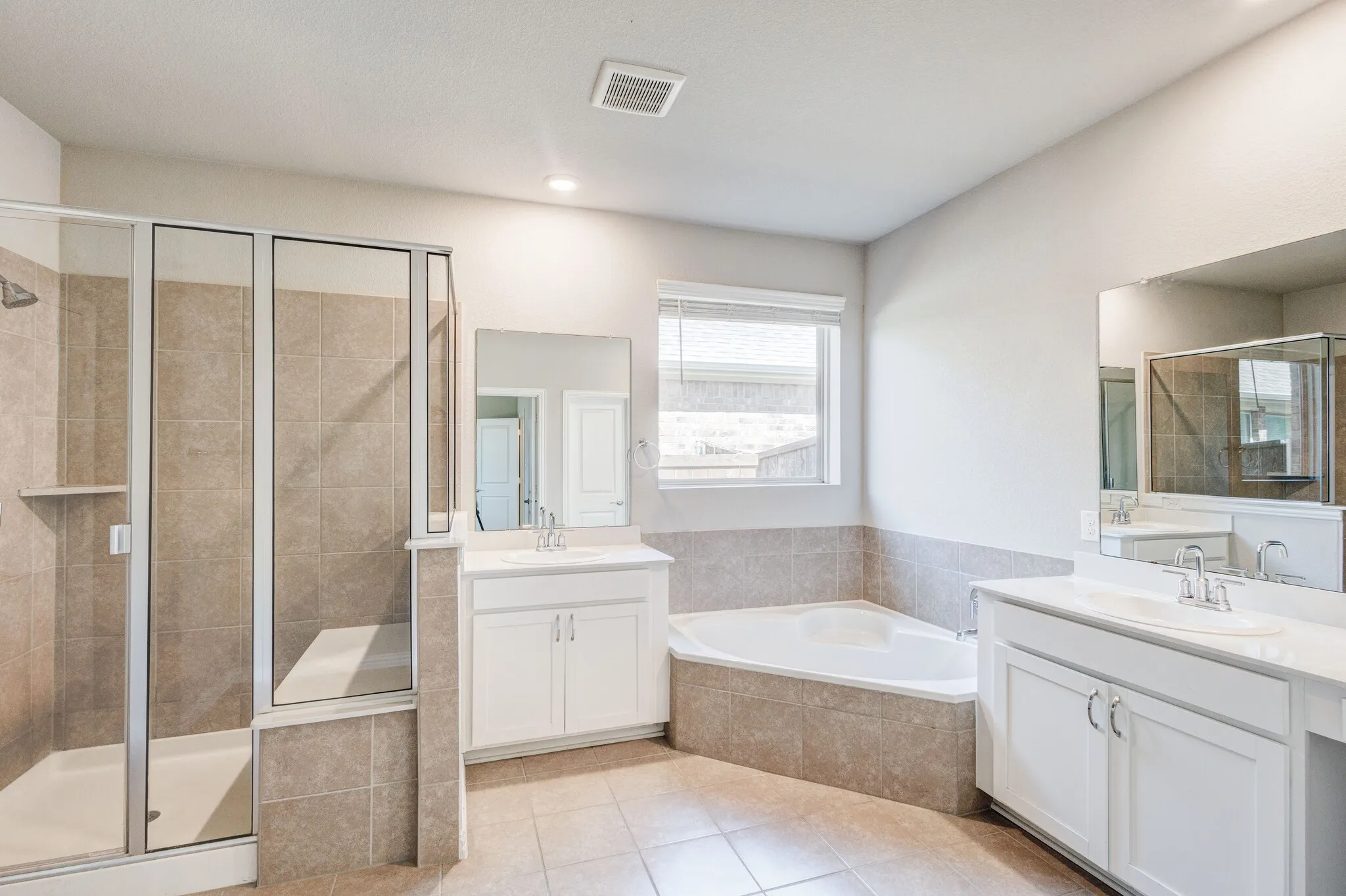 Tiled flooring leading to a walk-in shower with a built-in bench, a soaking tub, and dual vanities with white cabinetry