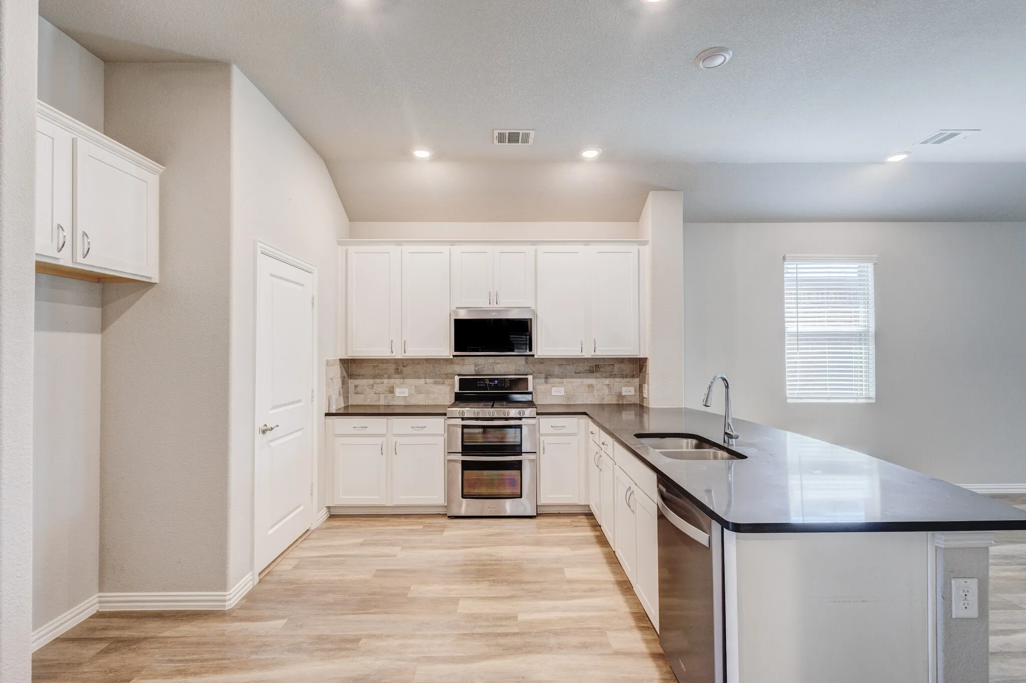 Kitchen featuring white cabinetry, stainless steel appliances, dark countertops, a tiled backsplash, and wood-finish flooring