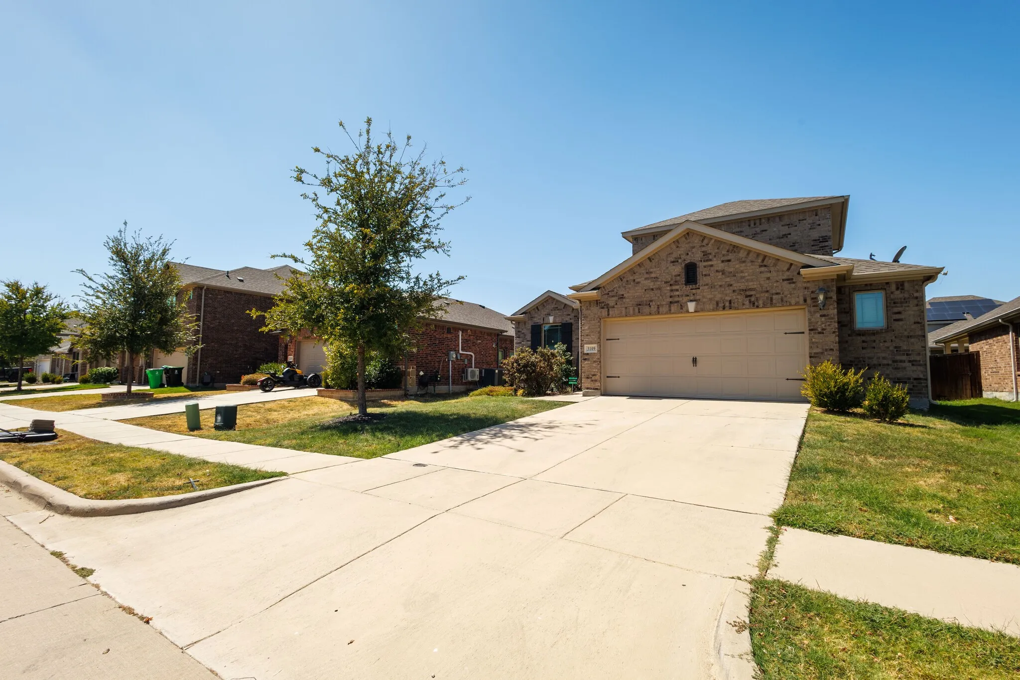 Brick exterior with an attached two-car garage, concrete driveway, and mature landscaping