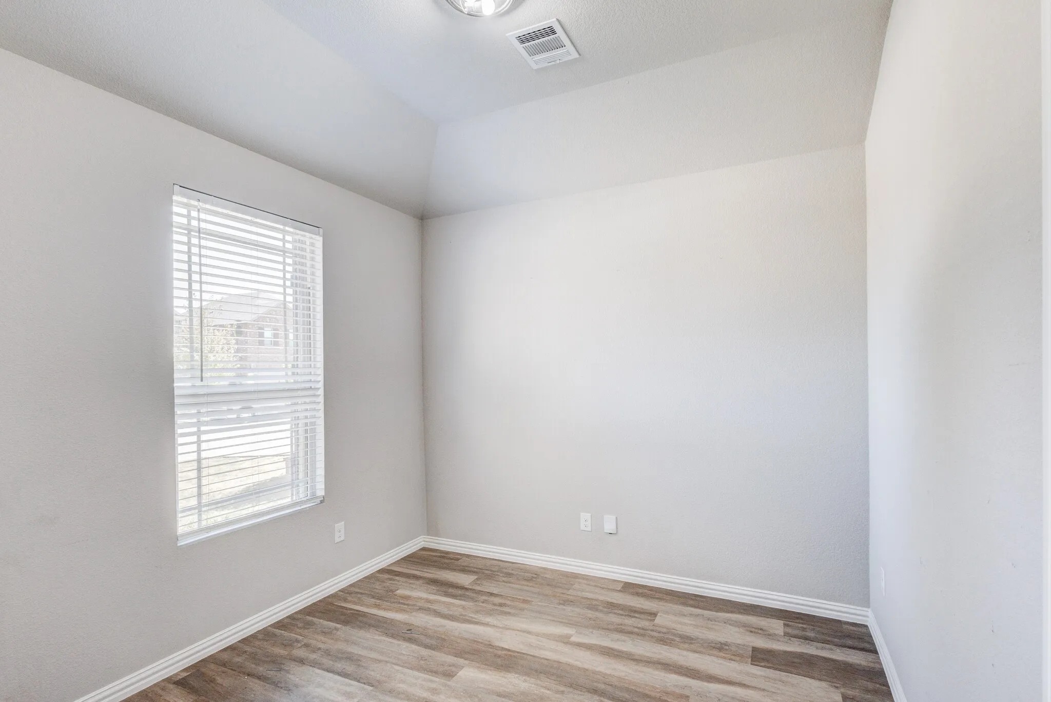 Light-filled room featuring a single window with blinds, wood-finish flooring, and light-toned walls