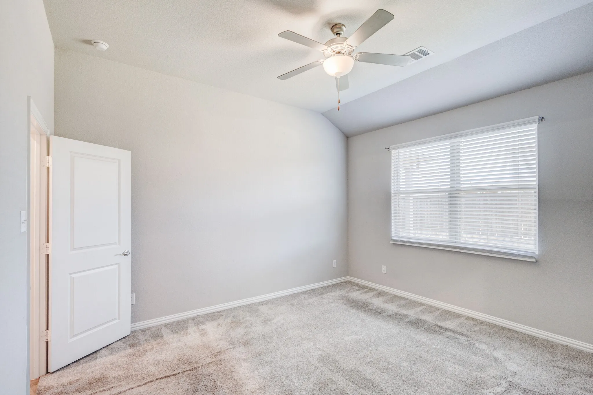 Vaulted ceiling, ceiling fan with integrated lighting, window with blinds, light-toned carpeting, and a paneled door