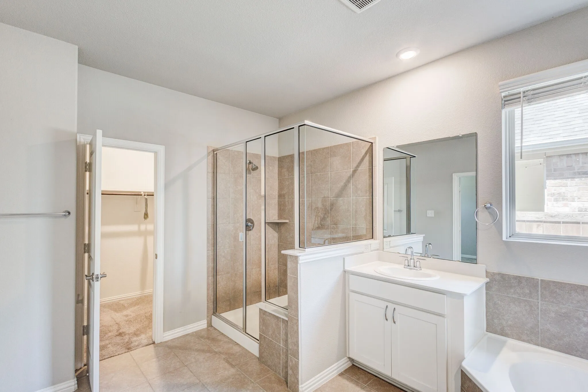 Full bathroom featuring a glass-enclosed shower with tiled surround, a built-in bathtub, a single vanity with a white countertop and cabinet storage, and tiled flooring