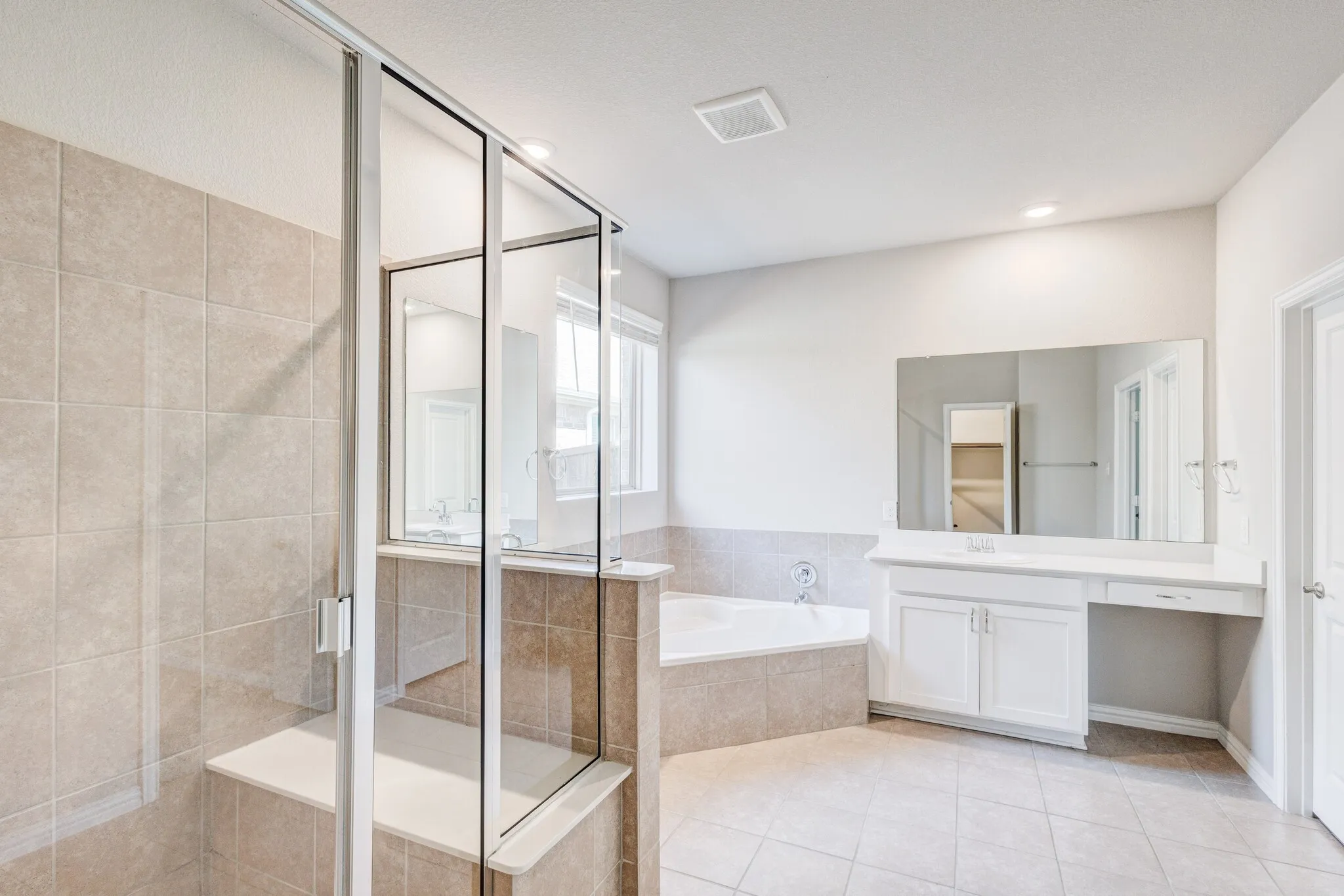 Glass-enclosed shower with a built-in bench, corner soaking tub, white vanity with integrated sink, and large wall-mounted mirror