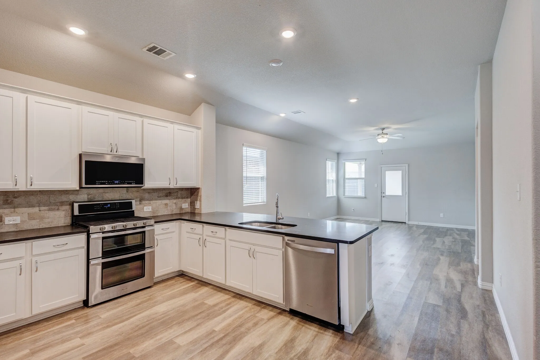 Kitchen featuring white shaker cabinetry, stainless steel appliances, dark countertops, and a stone-finish backsplash