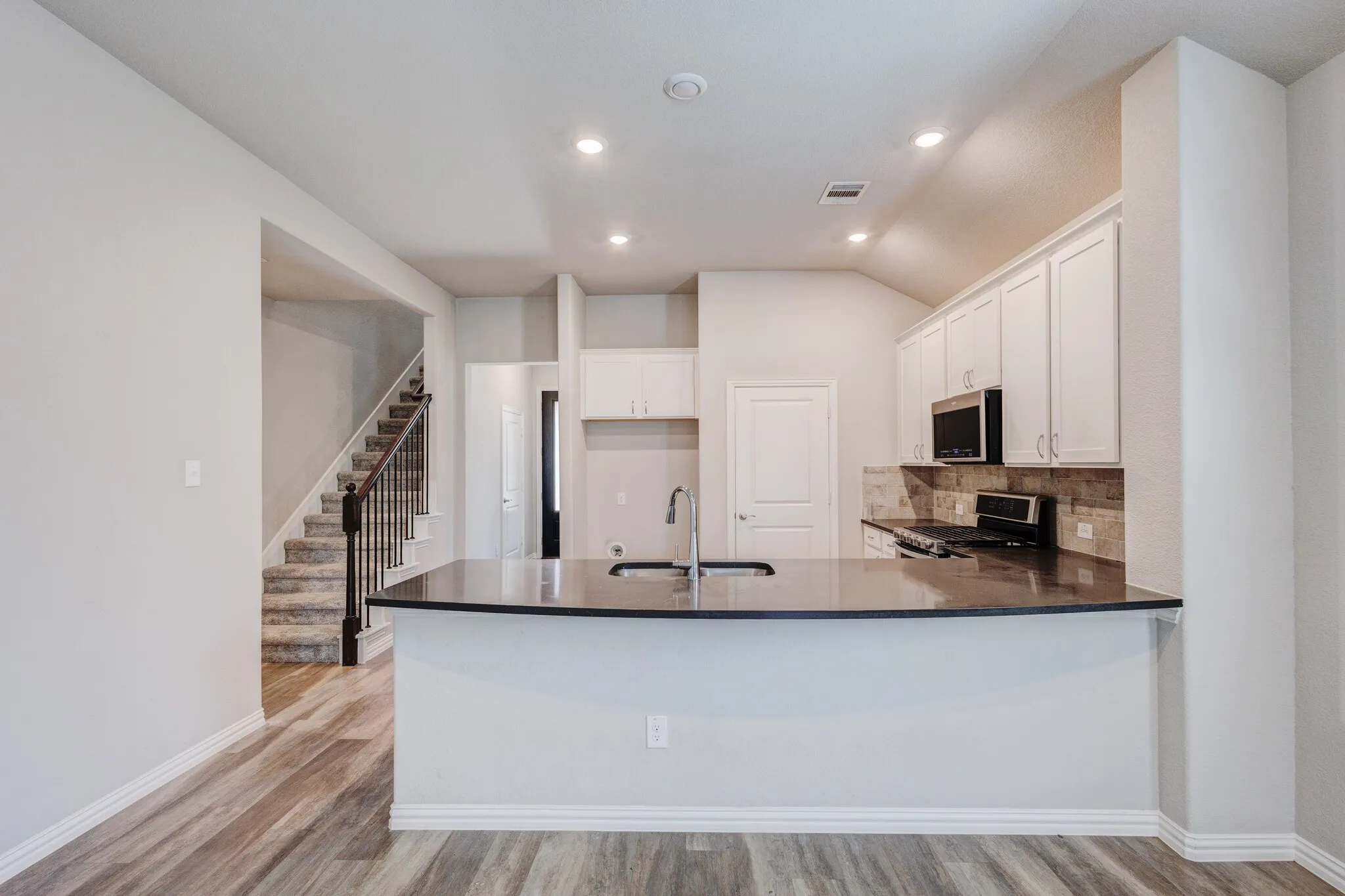 Kitchen island with dark countertop, white cabinetry, integrated sink, and wood-finish flooring